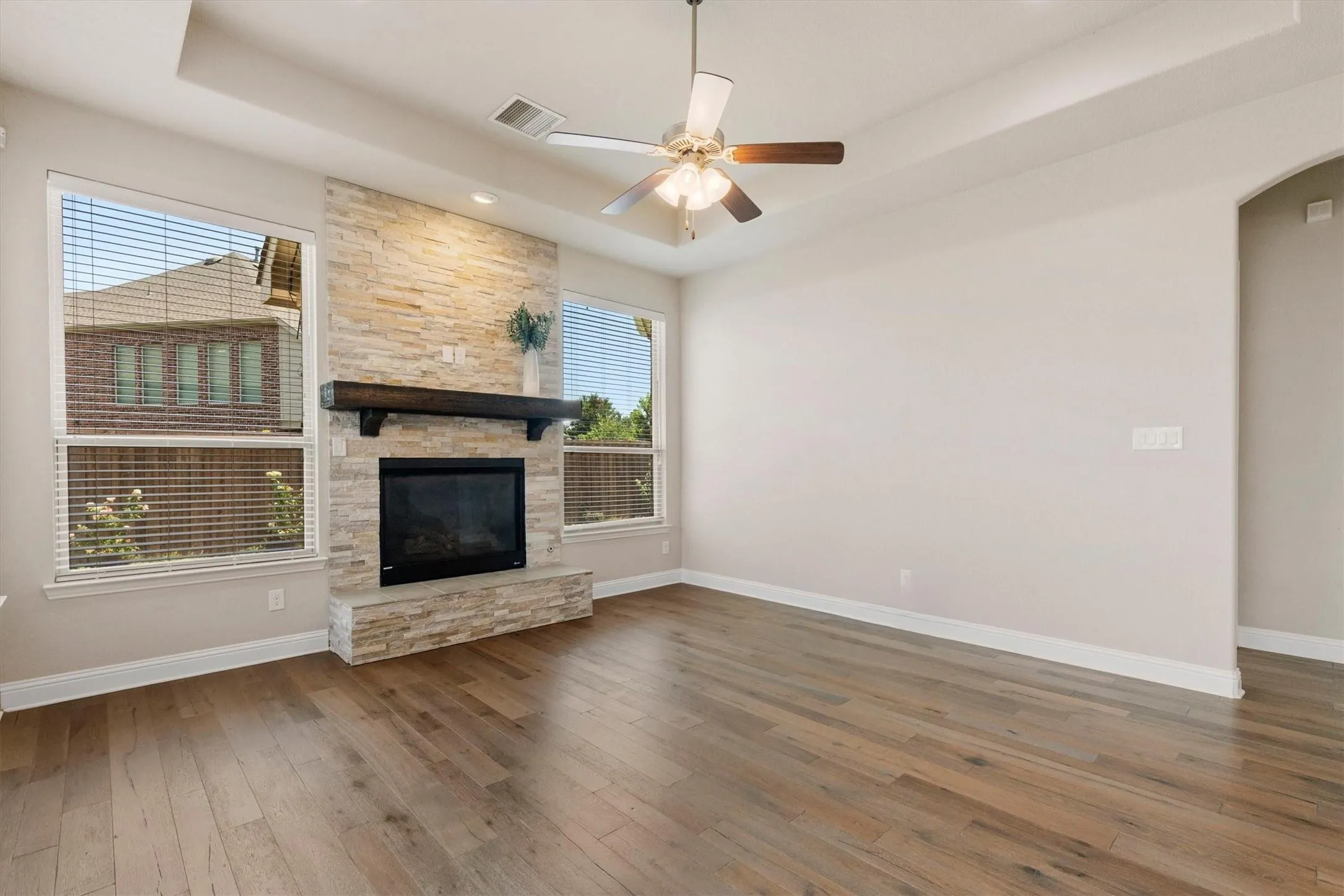 Stone-clad fireplace with a dark wood-finish mantel, wood-finish flooring, and a ceiling fan