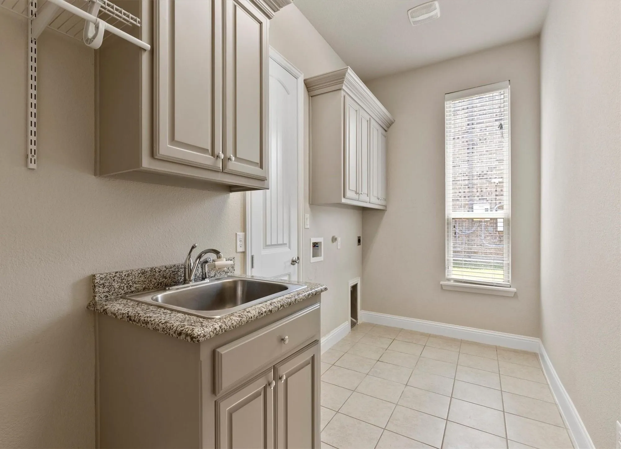 Utility room featuring granite-style countertop with undermount sink, soft-close cabinetry in neutral finish, ceramic tile flooring, and natural light from single-hung window