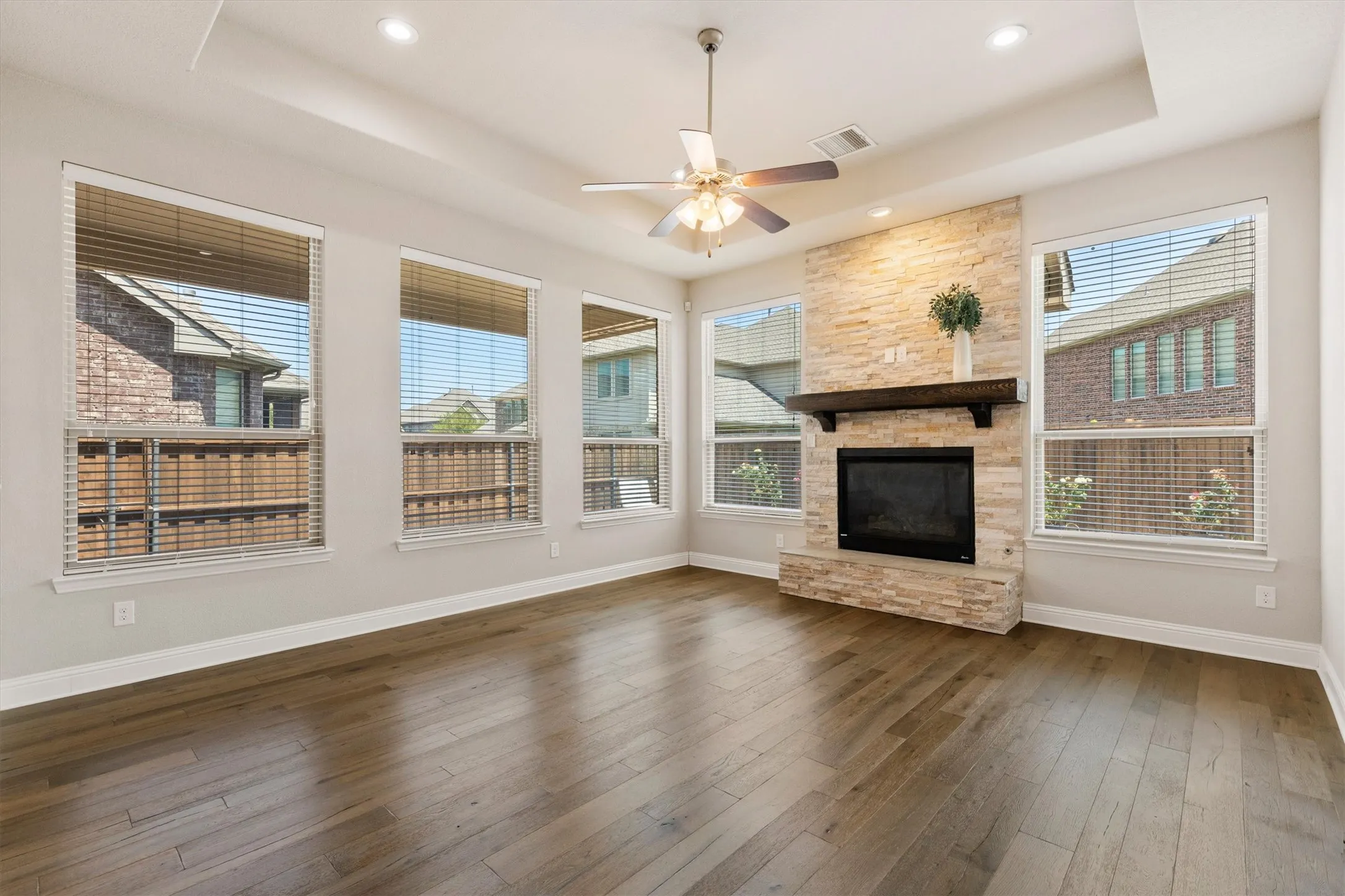 Stone-clad fireplace with a dark wood-finish mantel, wood-finish flooring, and a ceiling fan