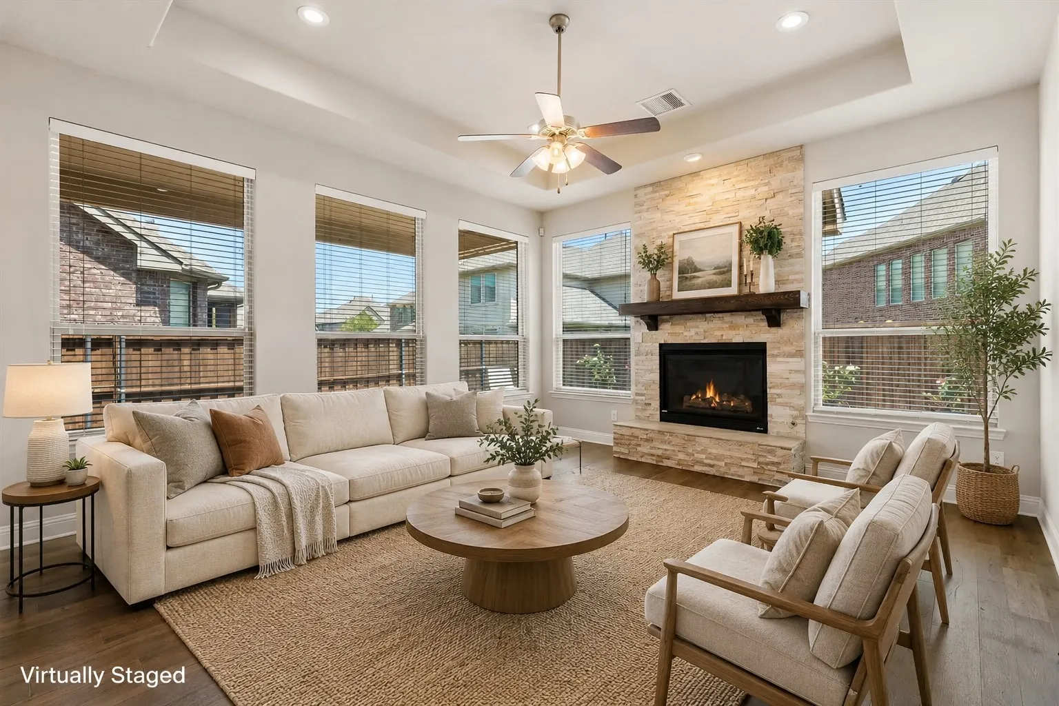 Spacious living area featuring a stone-faced fireplace with a wood mantel, multiple large windows, a ceiling fan, and wood-finish flooring
