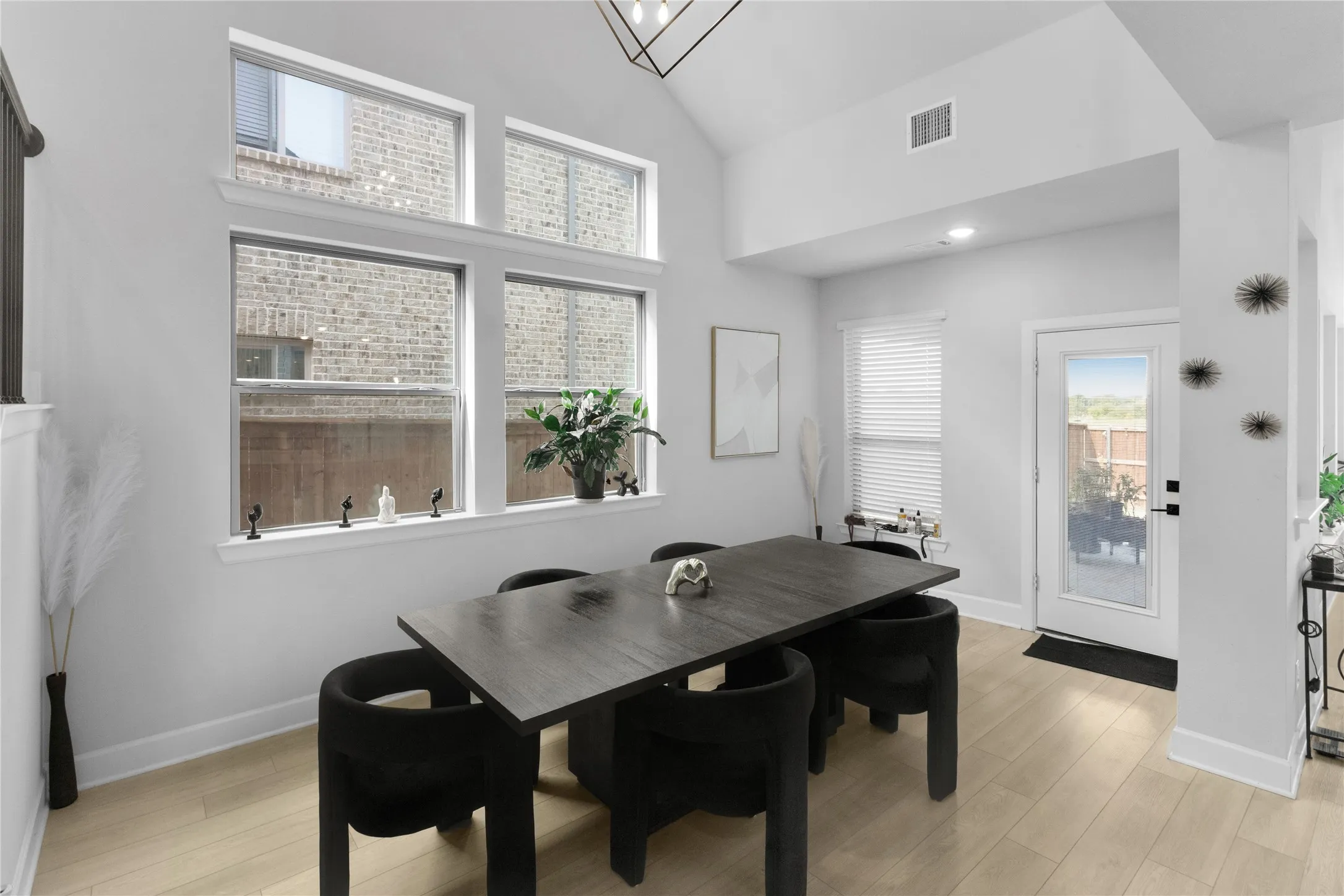 Dining area featuring a vaulted ceiling with contemporary lighting, light wood-finish flooring, and multiple windows providing natural illumination