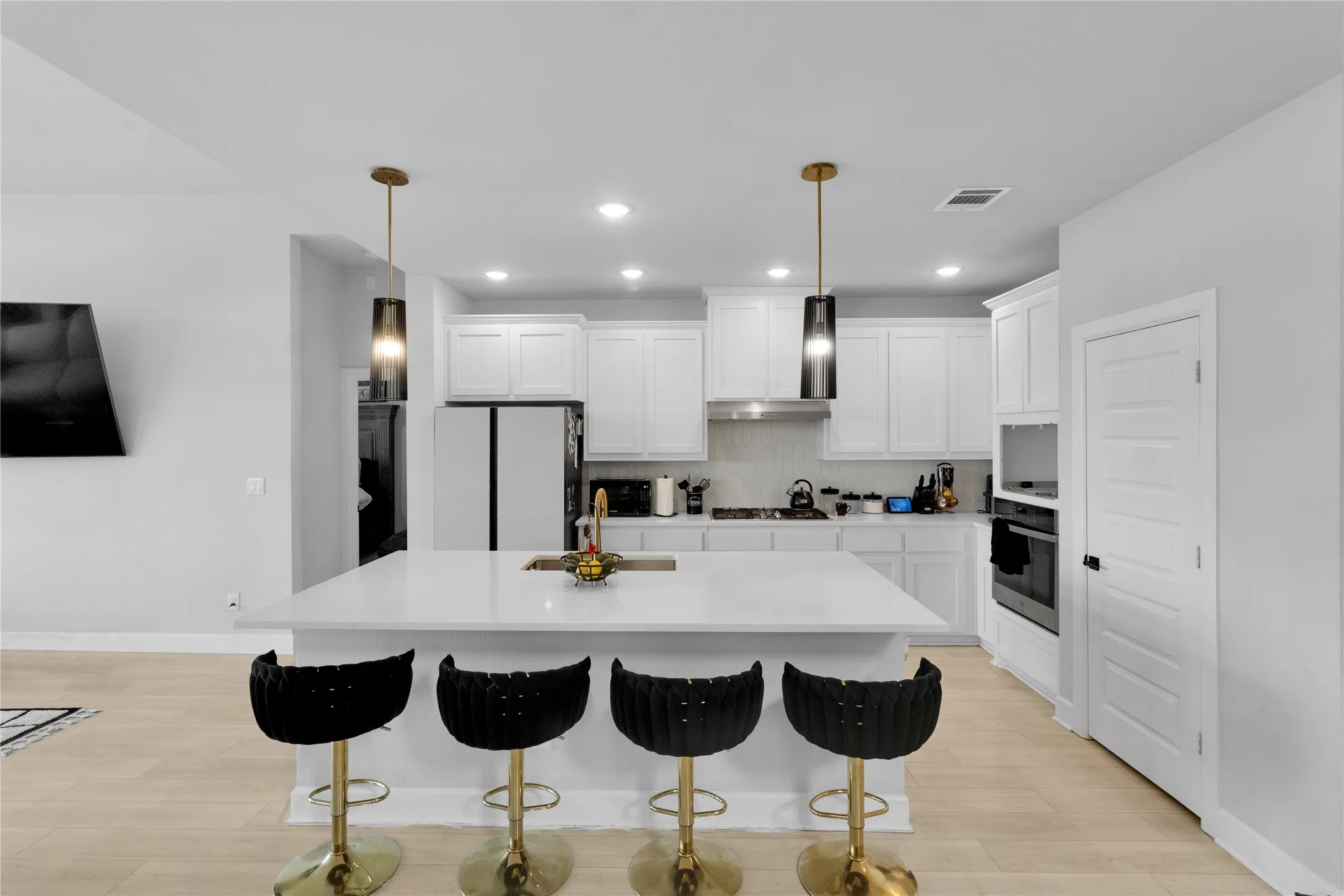 Contemporary kitchen featuring a large center island with integrated sink, white cabinetry, integrated stainless steel appliances, and wood-finish flooring