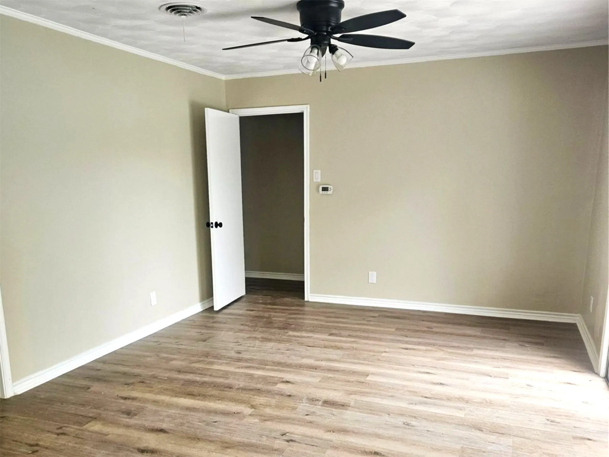Spacious room featuring wood-finish flooring, natural light, neutral wall paint, black matte finished ceiling fan with integrated lighting and crisp white baseboards