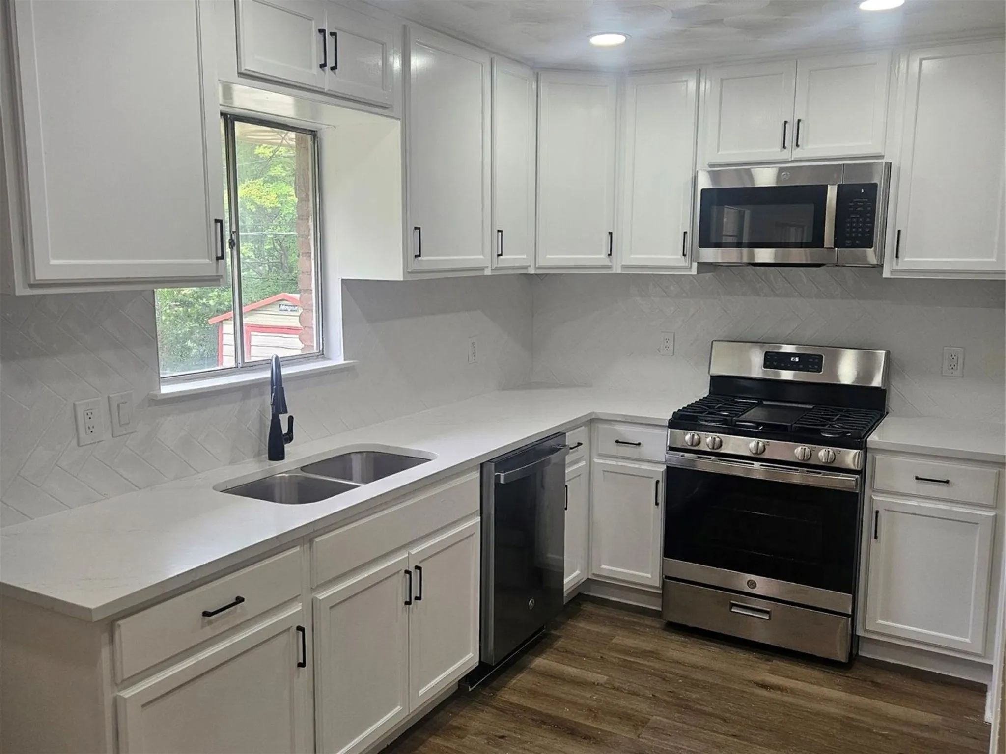 Kitchen featuring new white cabinets, stainless steel appliances, quartz countertops, a double basin sink with a matte black faucet, and wood-finish flooring