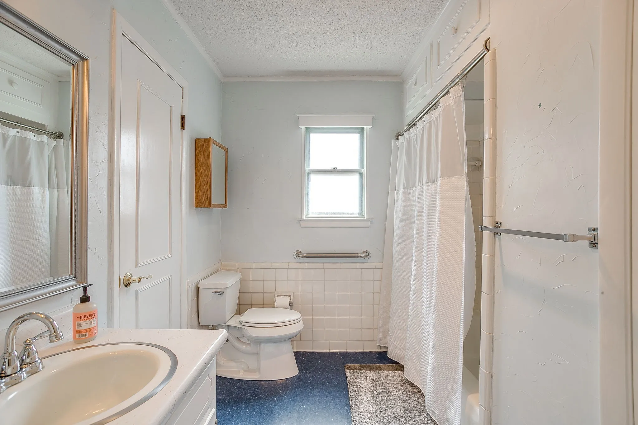 Bathroom featuring a window, white tile wainscoting, built-in medicine cabinet, and a chrome-framed vanity mirror