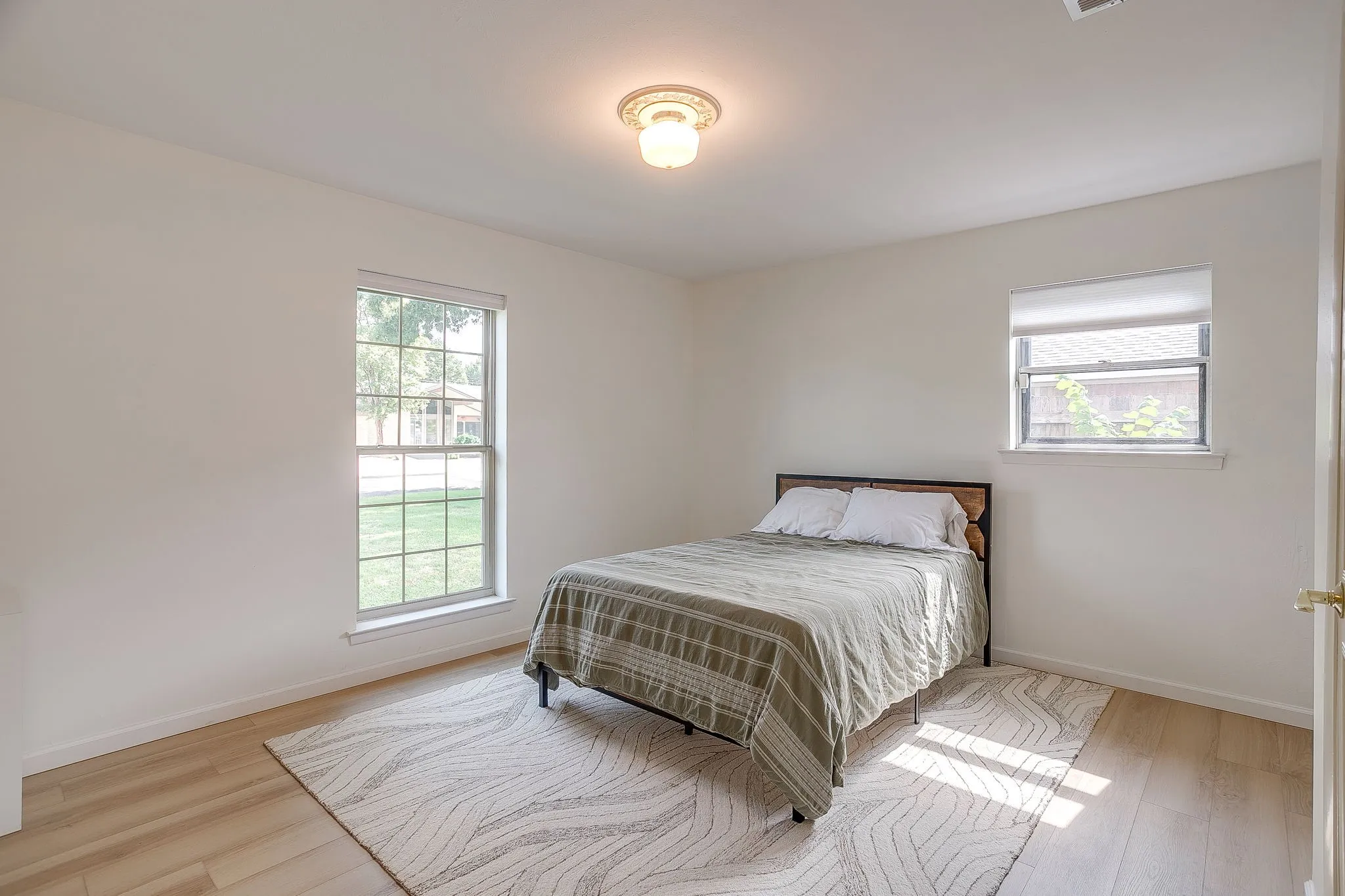 Light-filled room featuring wood-finish flooring, two windows, and a ceiling-mounted light fixture