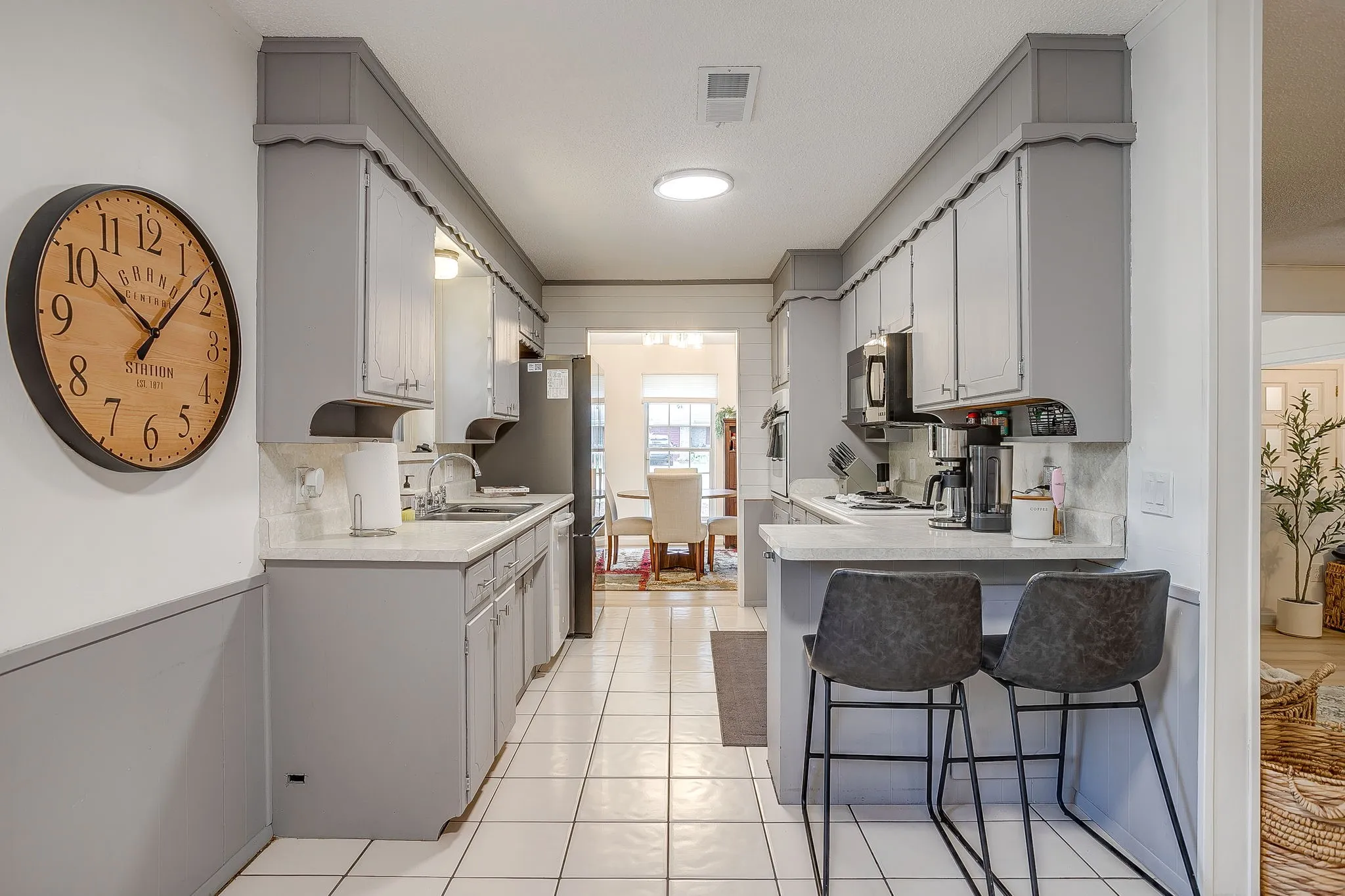 Galley kitchen featuring light gray cabinetry, light countertops, white tile flooring, and integrated appliances