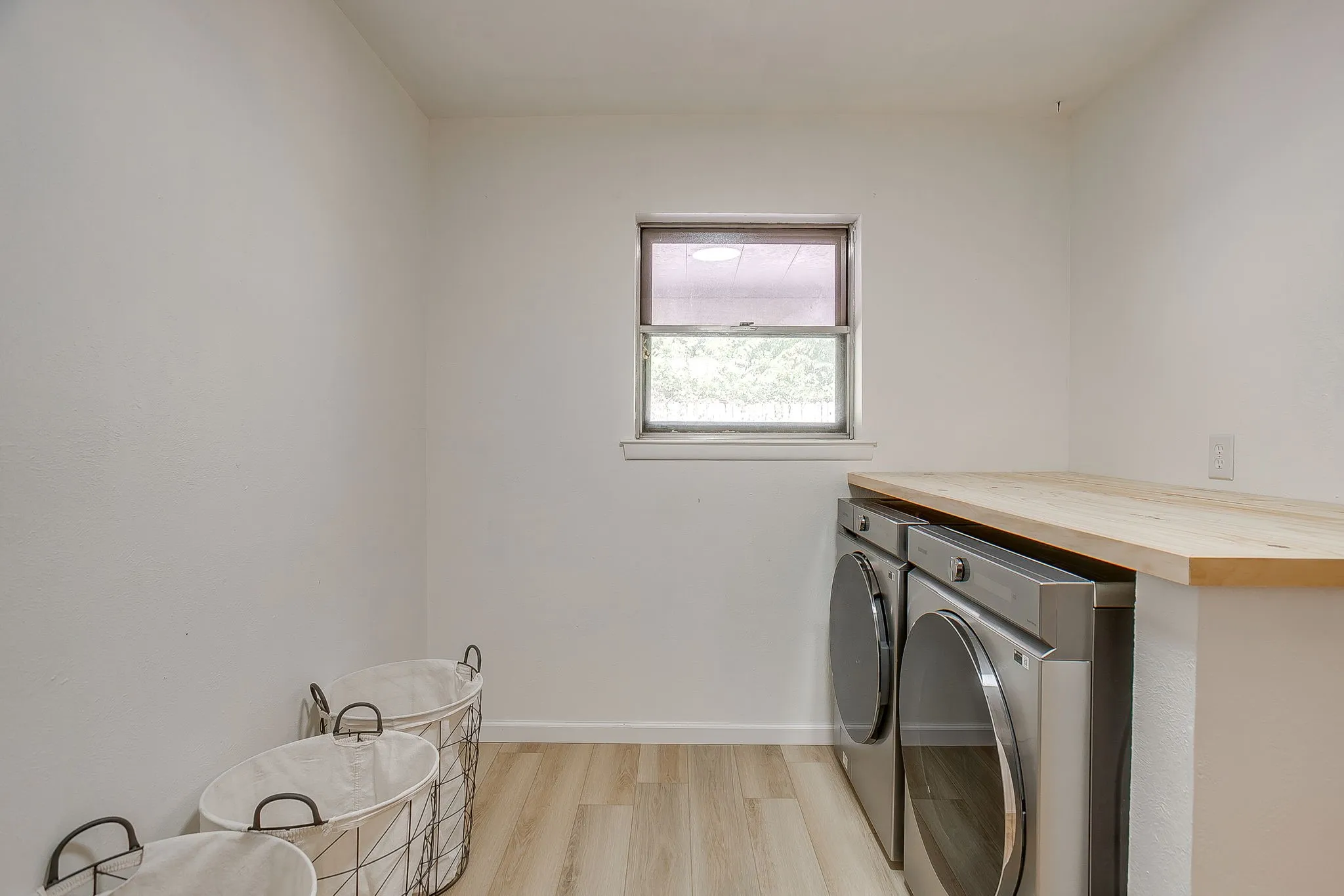 Window-equipped laundry area featuring wood-finish flooring and a light wood countertop