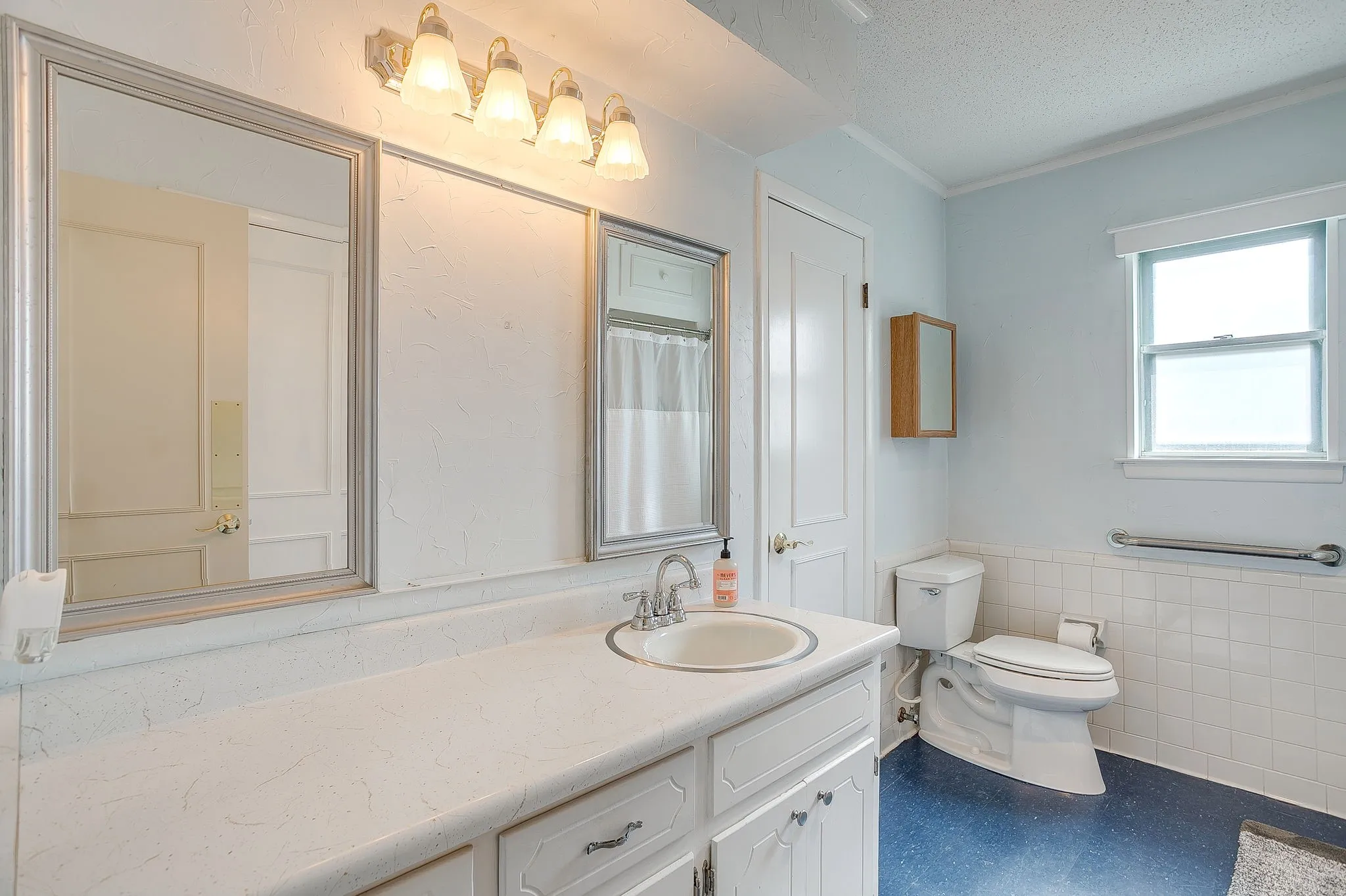 Spacious bathroom featuring a single vanity, framed mirror, wall-mounted light fixture, and window