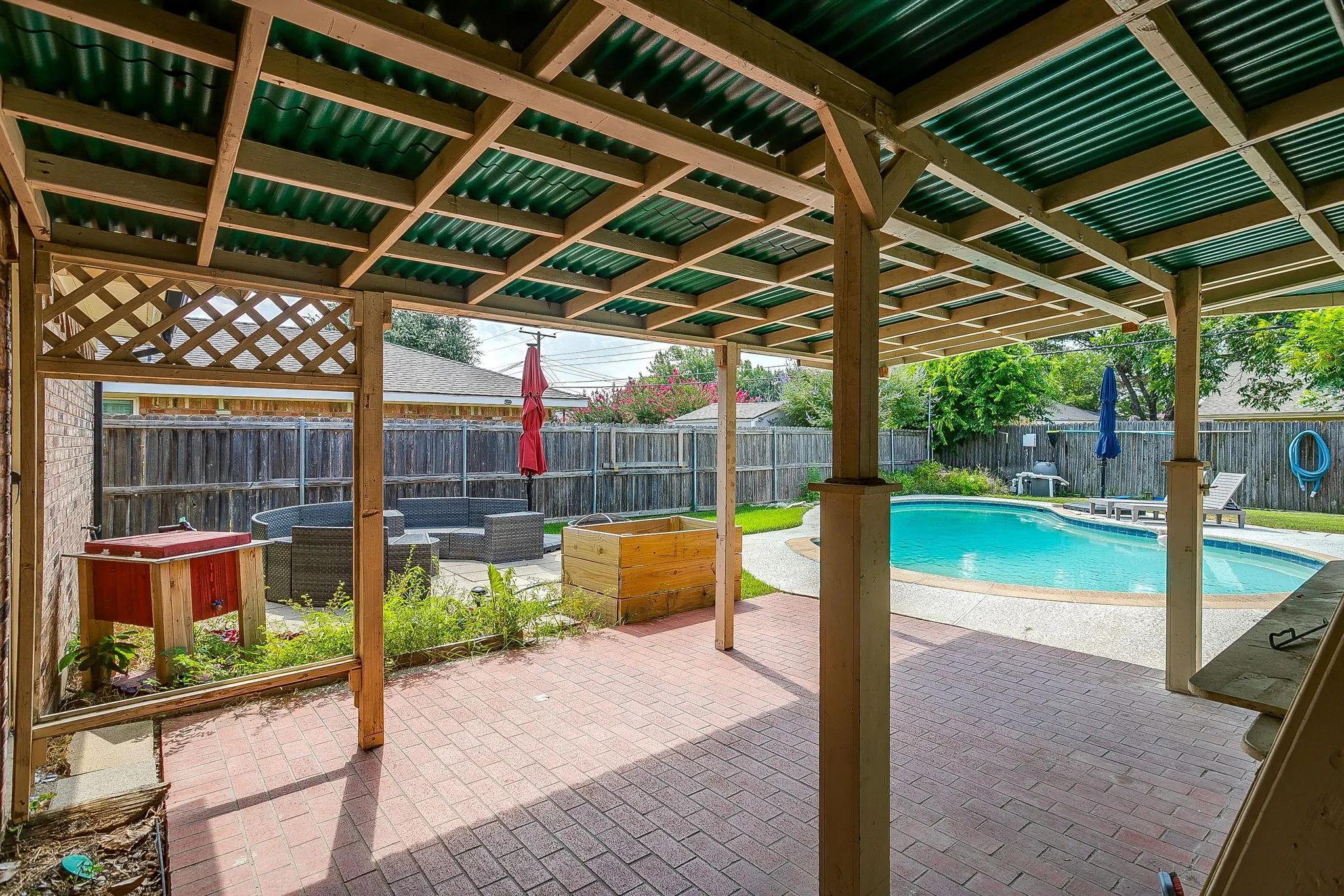 Covered patio with a corrugated roof, brick paver flooring, and lattice detailing