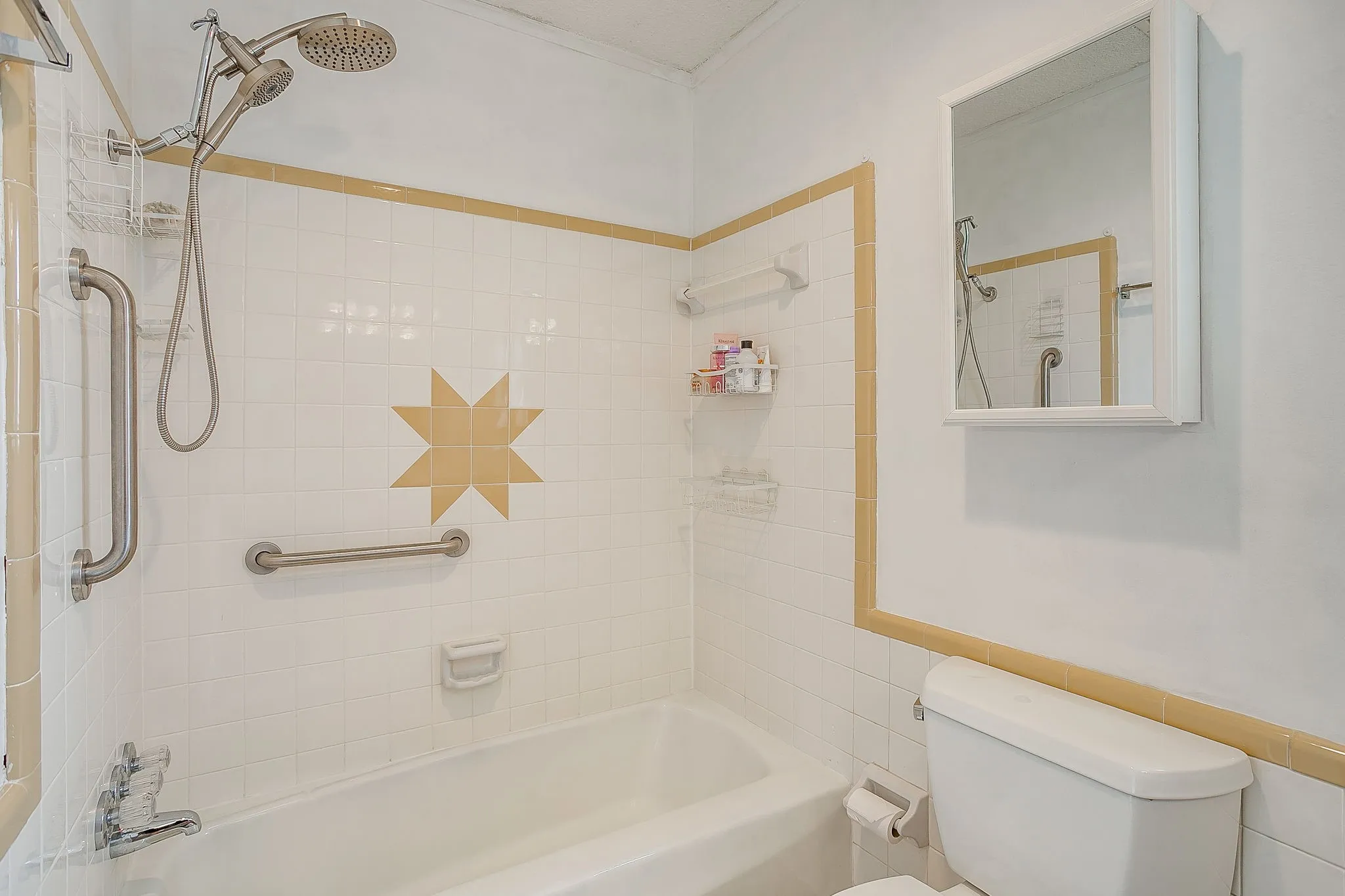 Bathtub with white tile surround, decorative accent tile, and satin nickel grab bars