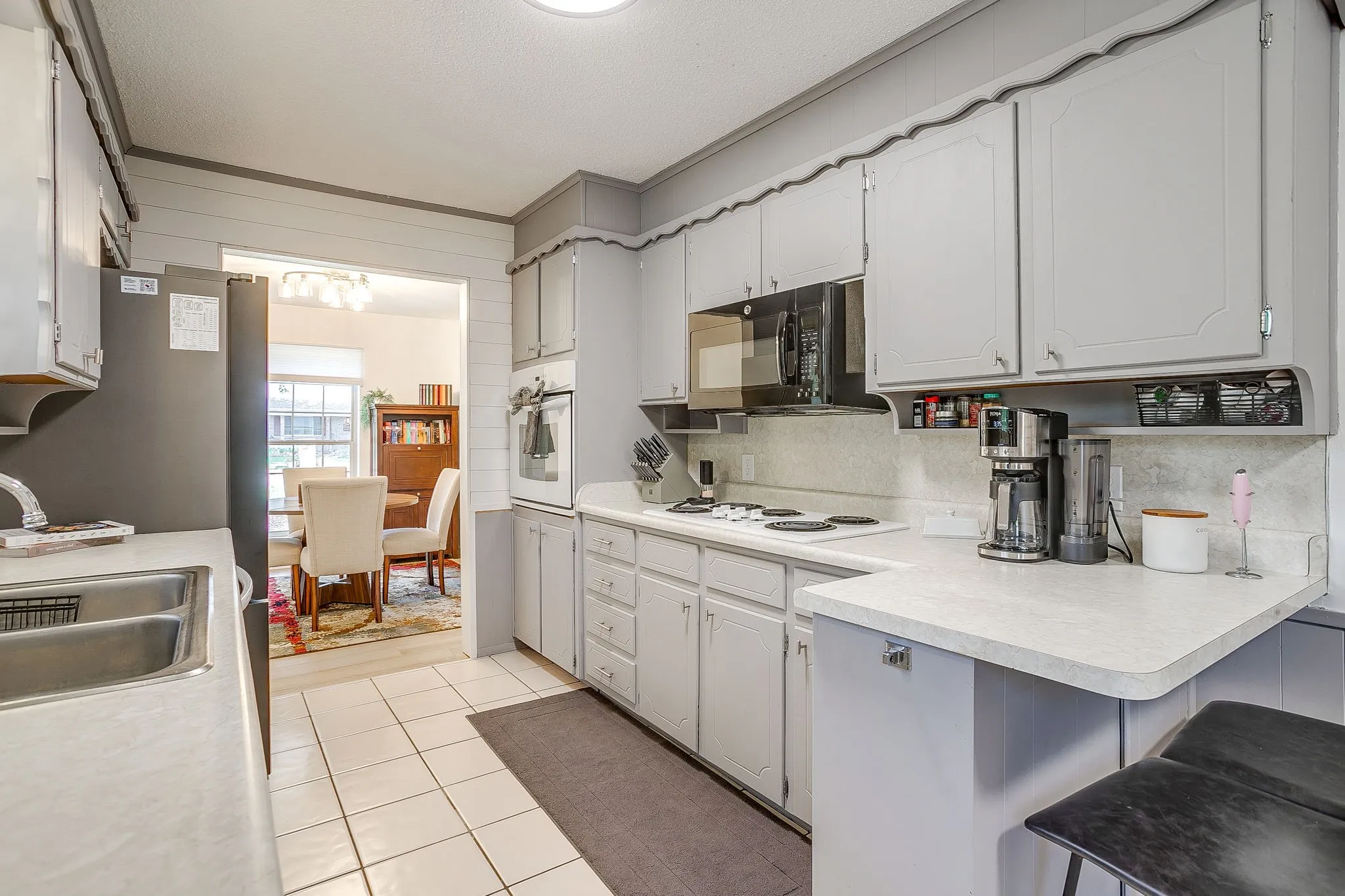Kitchen featuring light grey cabinetry, a stainless steel double basin sink, white countertops, a built-in microwave, and tile flooring