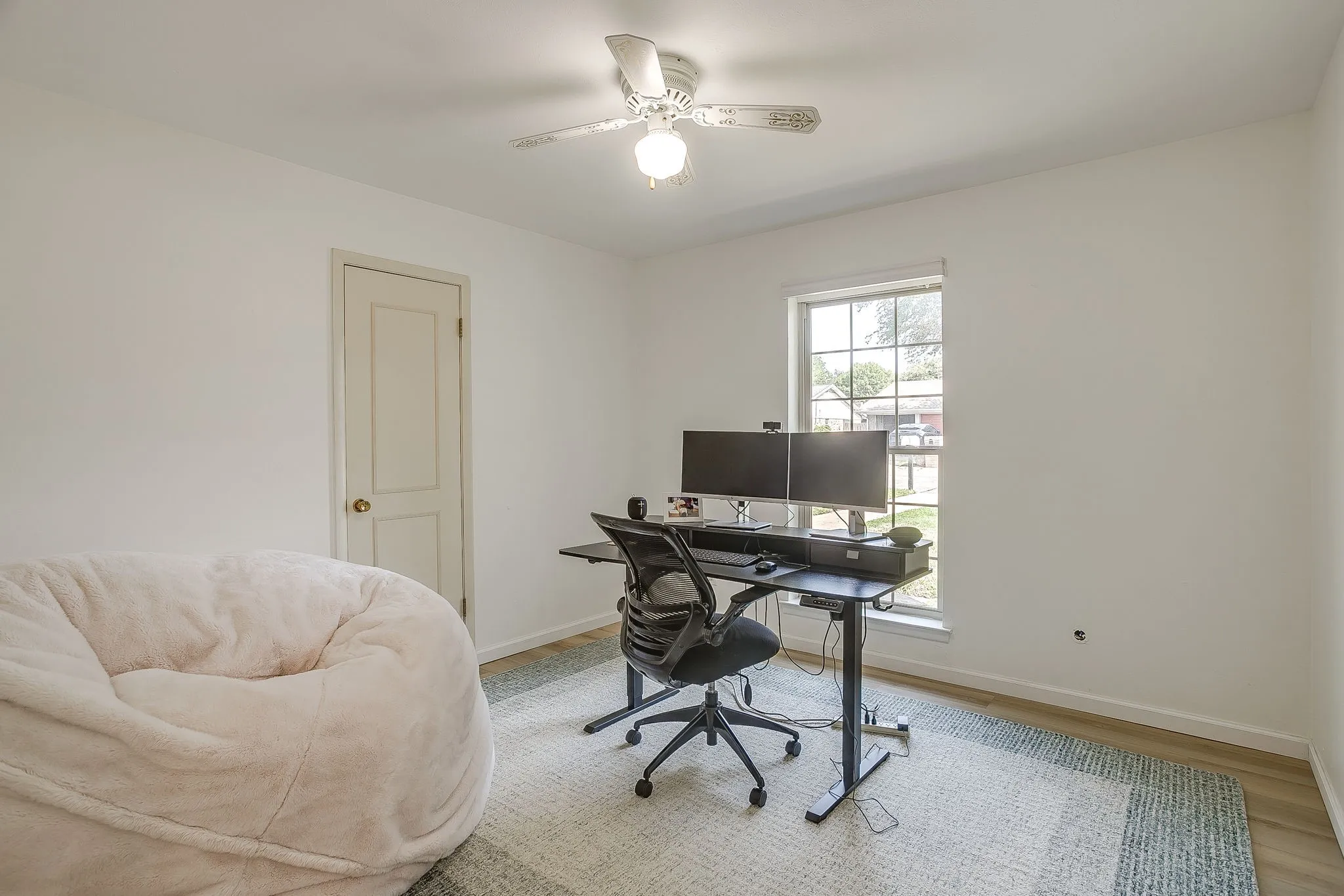 Ceiling fan with integrated lighting, wood-finish flooring, white painted walls, and a window providing natural light