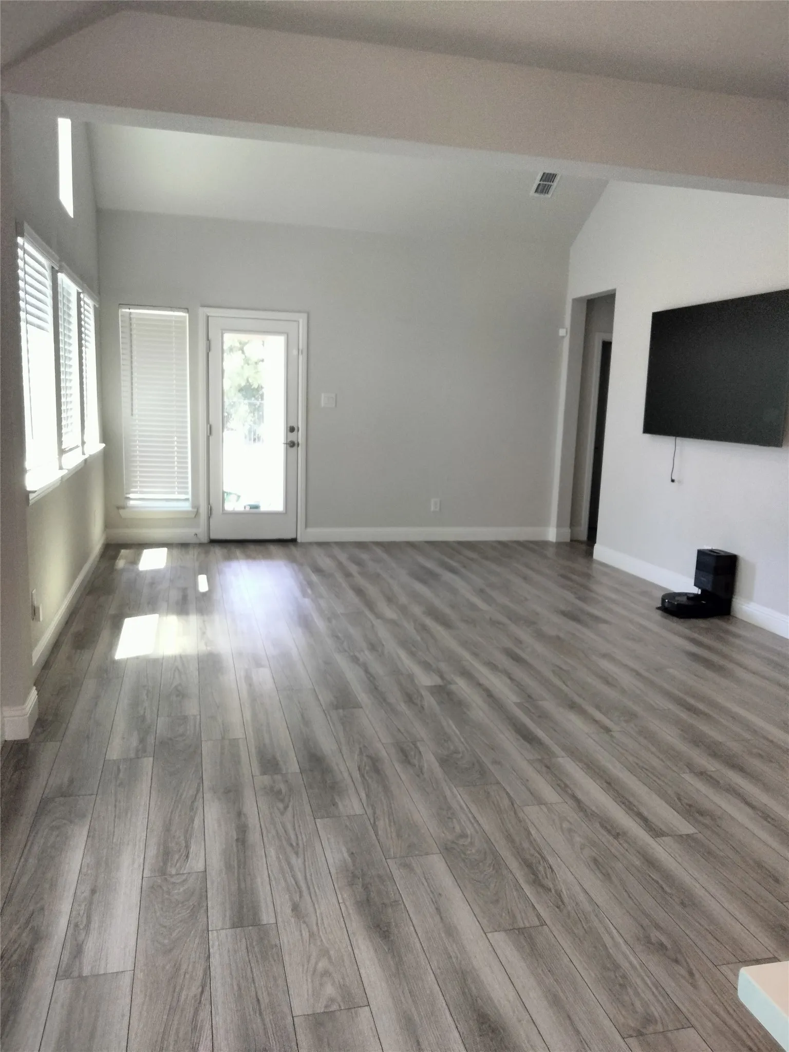 Vaulted ceiling, wood-finish flooring, multiple windows with blinds, and a glass-paneled door