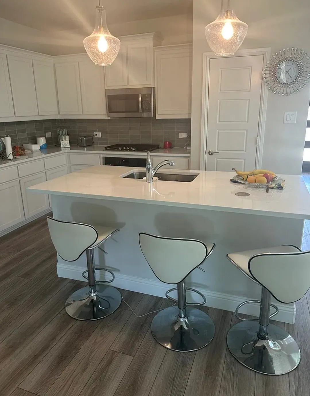 Kitchen featuring white shaker cabinetry, stainless steel appliances, a center island with sink, pendant lighting, and wood-finish flooring