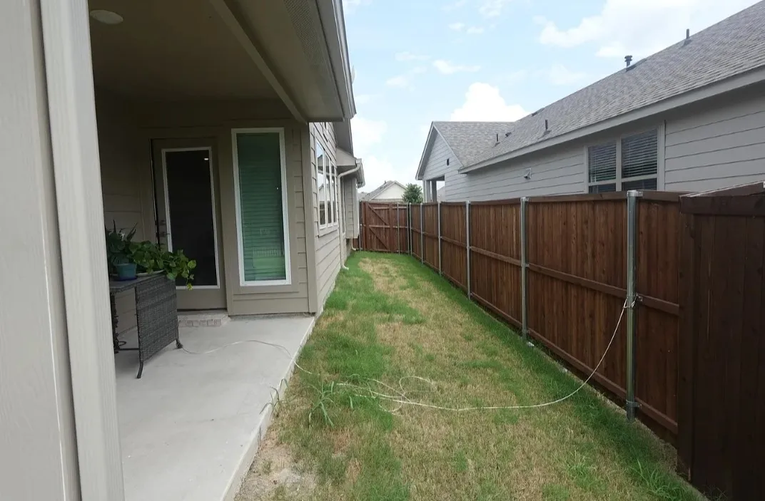 Covered concrete patio with exterior door and windows, alongside a grassy area with a wood privacy fence