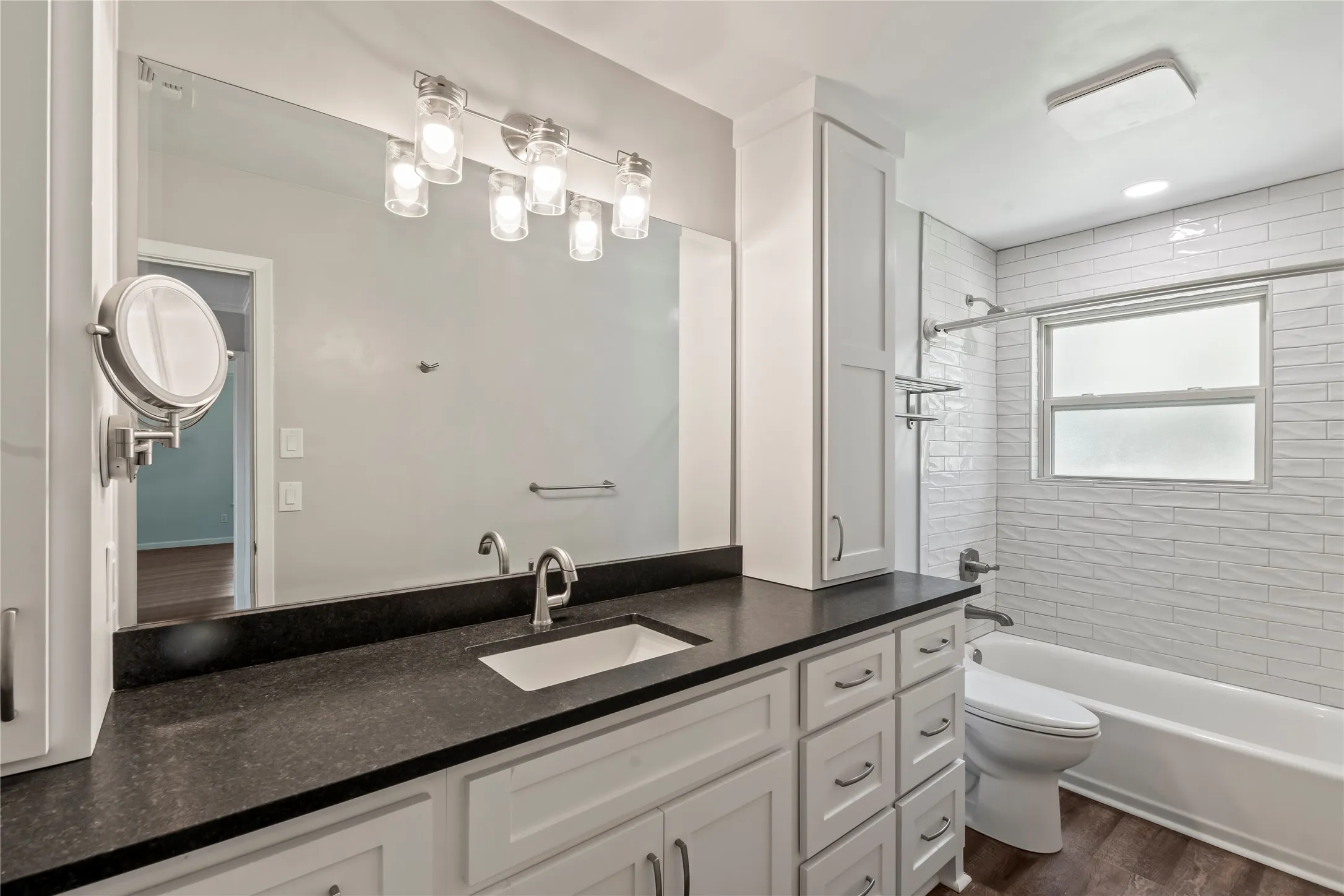Fully remodeled second bathroom featuring a tile tub and shower combination, black leather granite countertop, and ample storage.