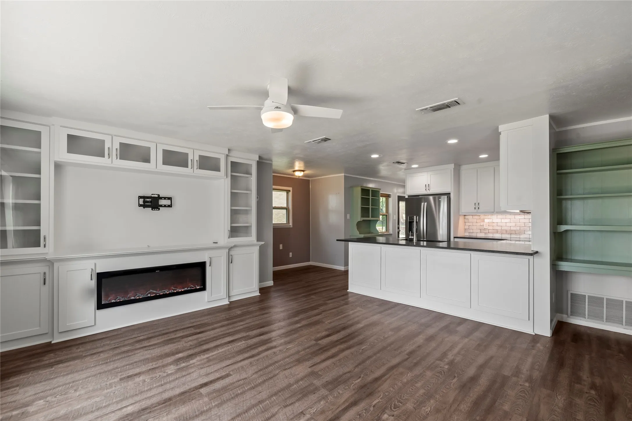 Open-concept living area showcasing the custom built-in entertainment center with electric fireplace and seamless flow into the kitchen.