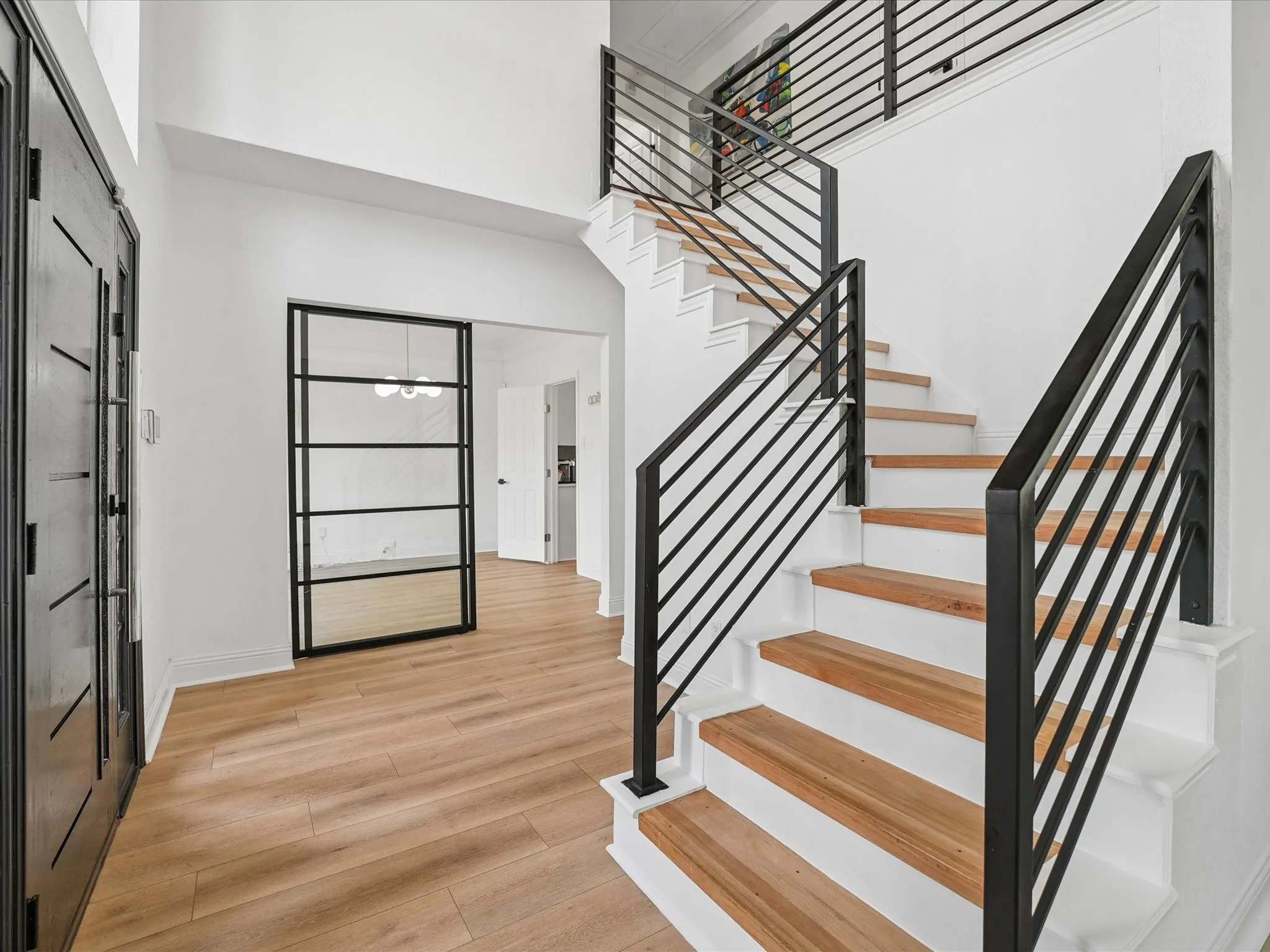Entryway featuring a modern staircase with wood-finish treads and black metal railings, a full-lite glass panel door with black trim, and wood-finish flooring