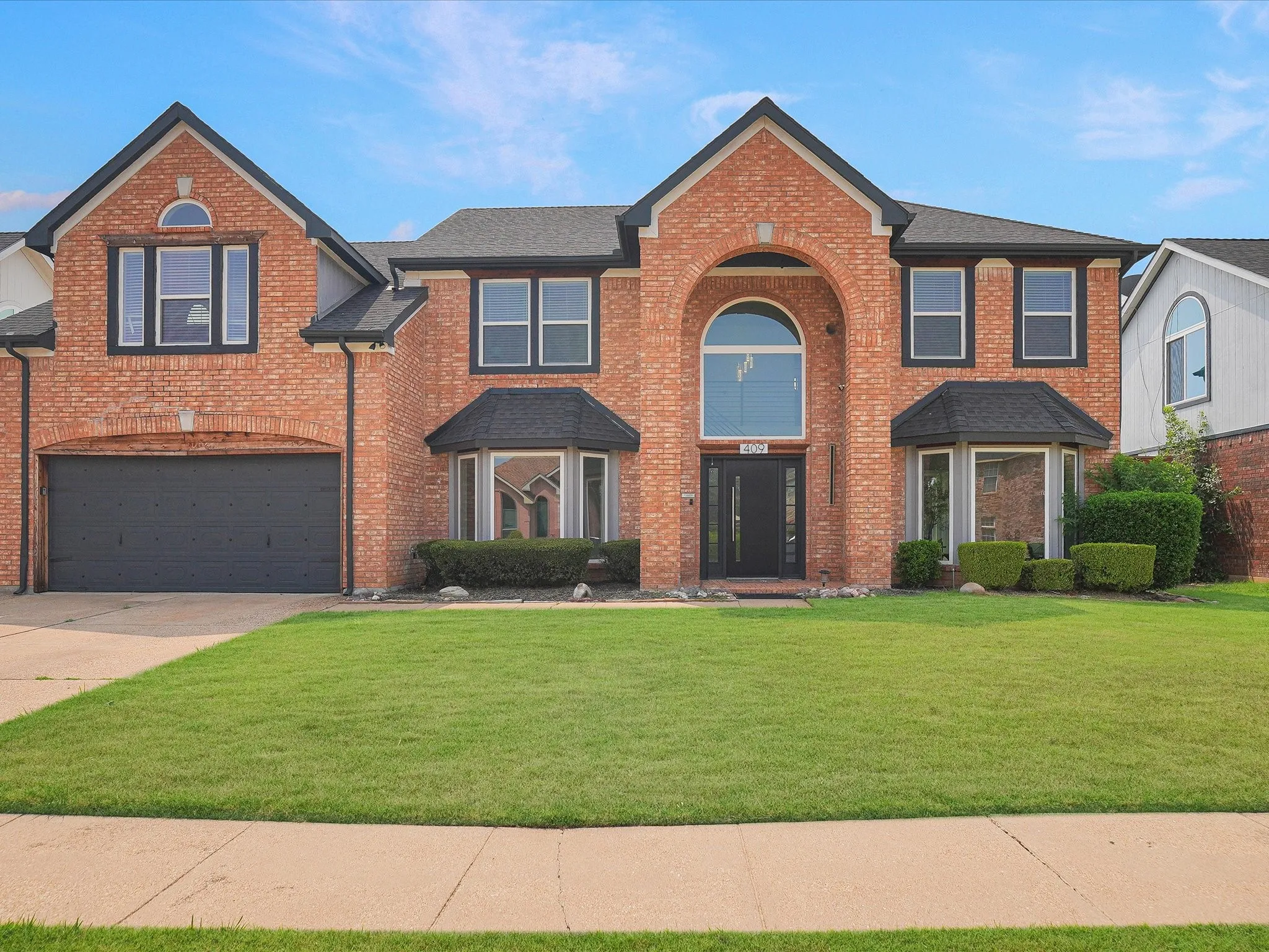Brick two-story residence featuring a prominent arched entryway with an oversized window
