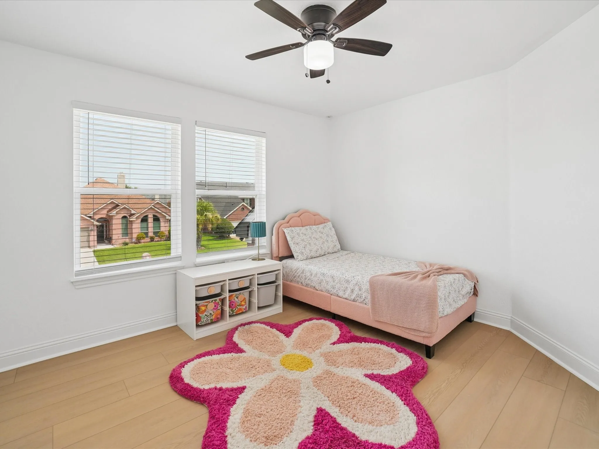 Bright room featuring two windows with horizontal blinds, light wood-finish flooring, a contemporary ceiling fan with integrated lighting, white baseboards, and neutral wall tones