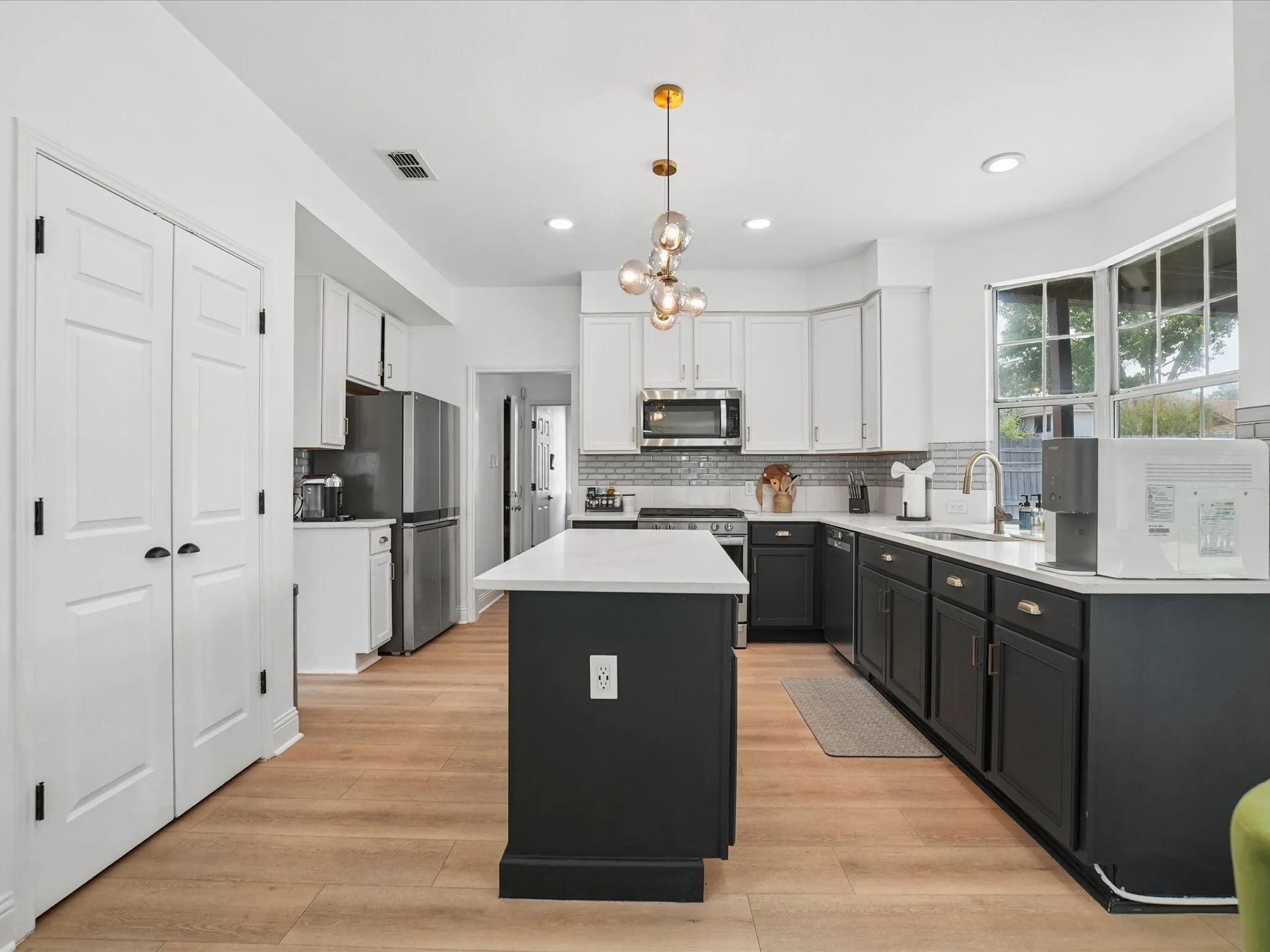 Kitchen featuring a central island with a white countertop, two-tone cabinetry, stainless steel appliances, wood-finish flooring, and a modern chandelier