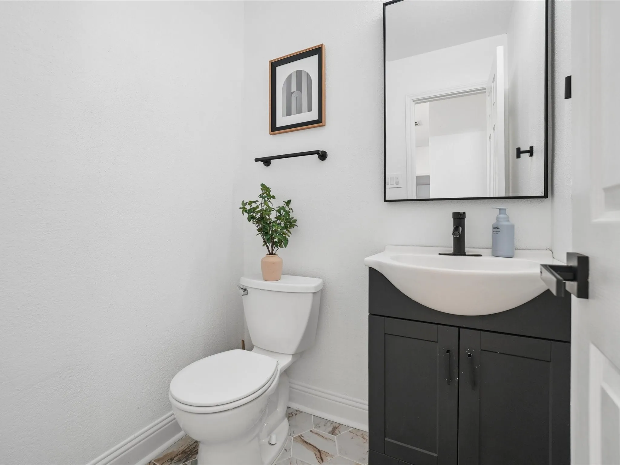 Modern powder room featuring a sleek black vanity with an integrated white ceramic sink, matte black wall-mounted faucet, and ample storage