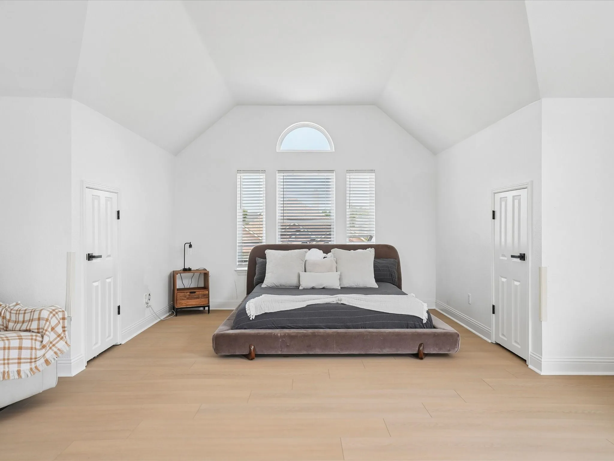 Vaulted ceilings with a prominent arched window, two paneled doors with black hardware, light wood-finish flooring, and crisp white baseboards