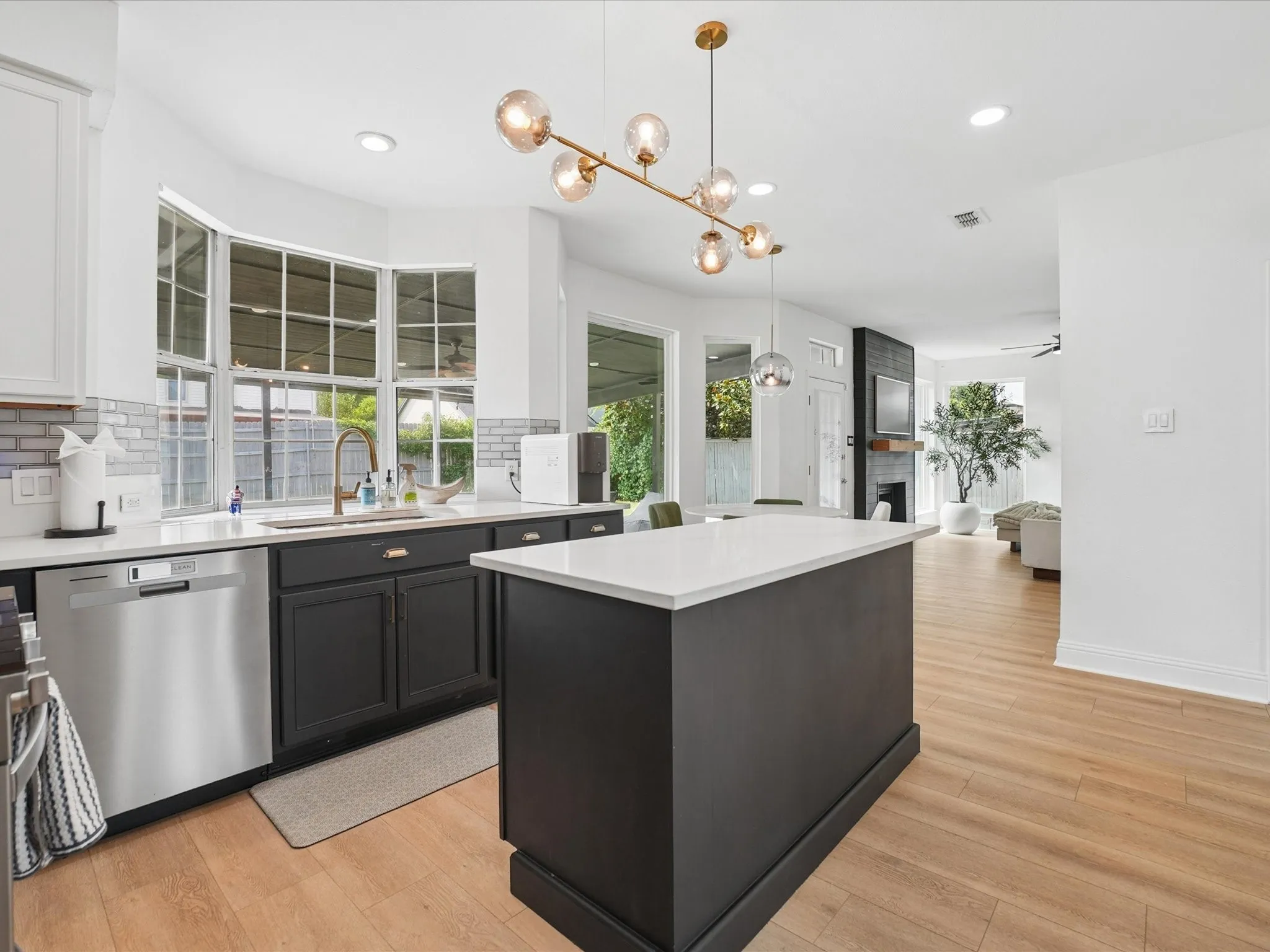 Contemporary kitchen featuring a central island with a white countertop, dark cabinetry, stainless steel appliances, and a stylish multi-bulb light fixture
