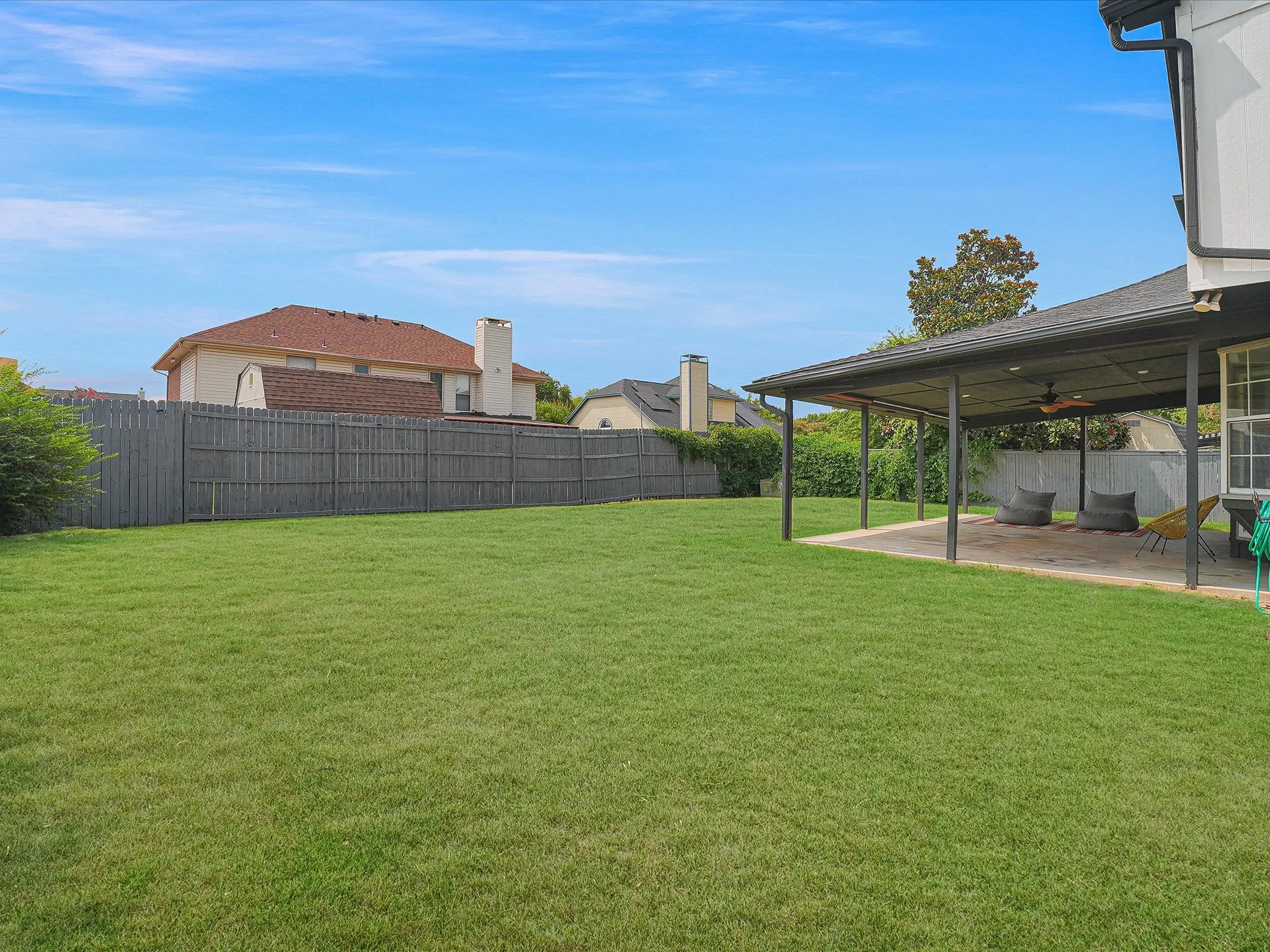 Expansive green lawn with a covered patio featuring a ceiling fan and recessed lighting