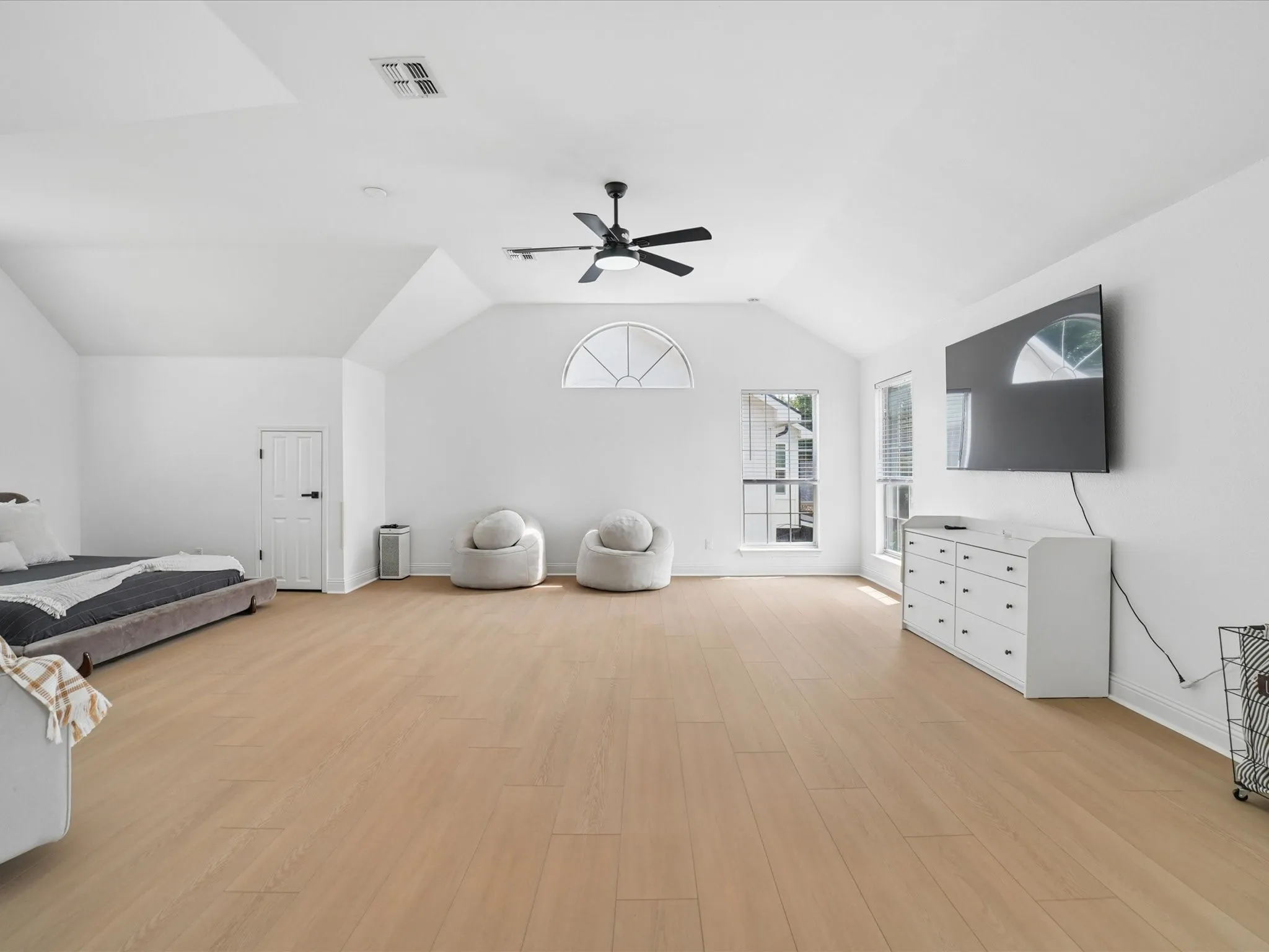 Spacious room featuring vaulted ceilings, light wood-finish flooring, and crisp white walls