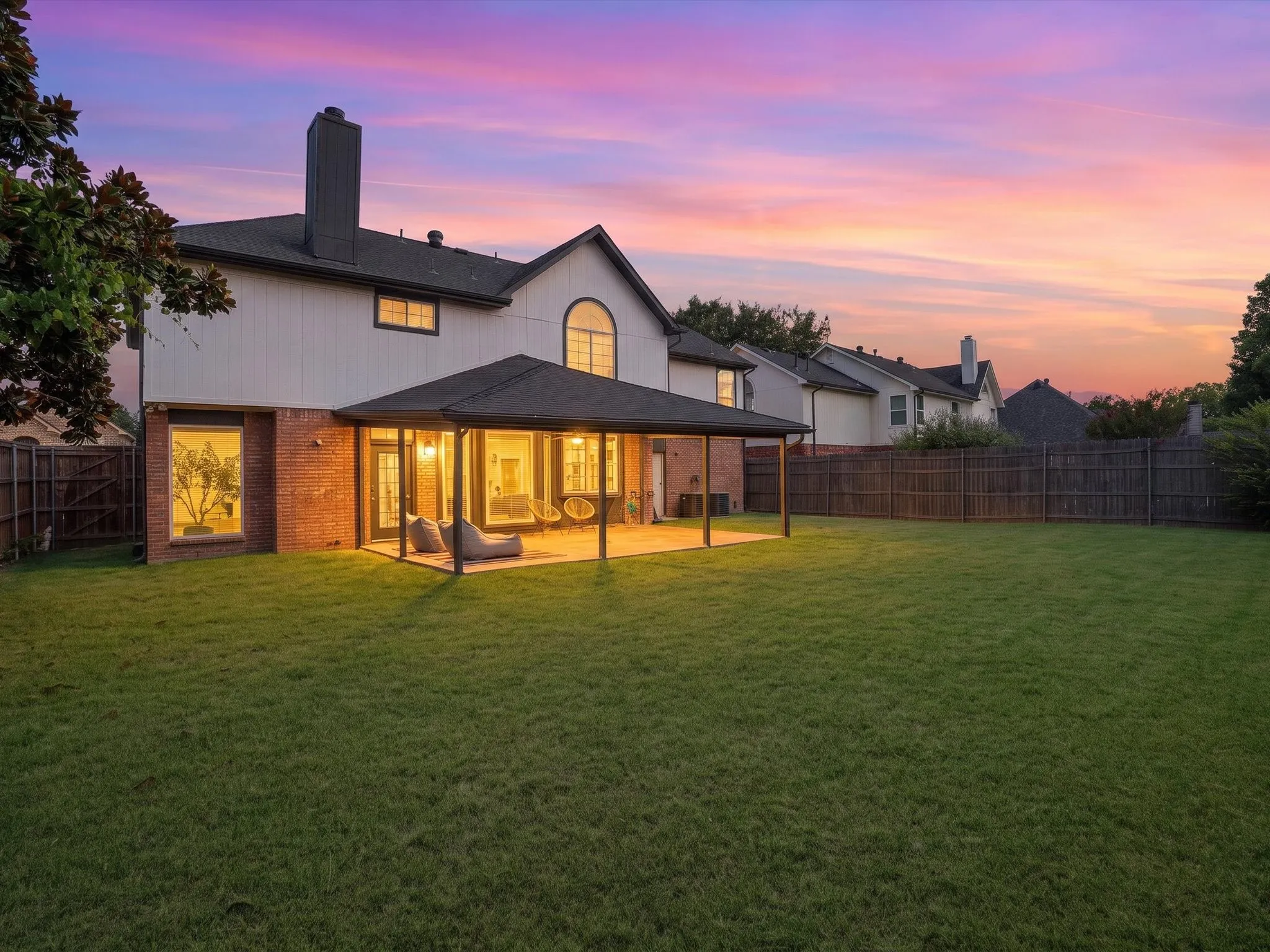 Expansive grassy backyard featuring a covered patio with integrated lighting