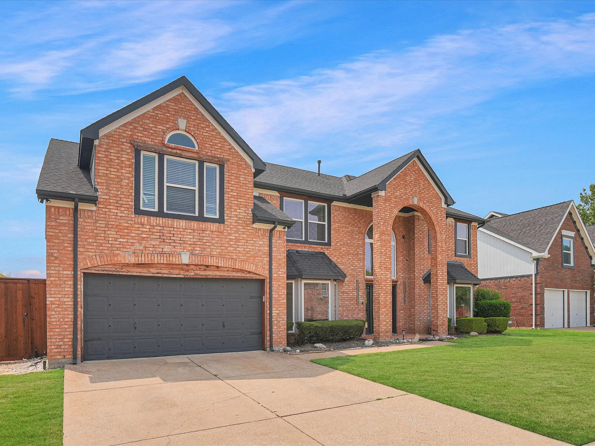 Traditional brick exterior featuring an arched entryway, gabled rooflines, dark framed windows, an integrated garage with a dark door, and a concrete driveway