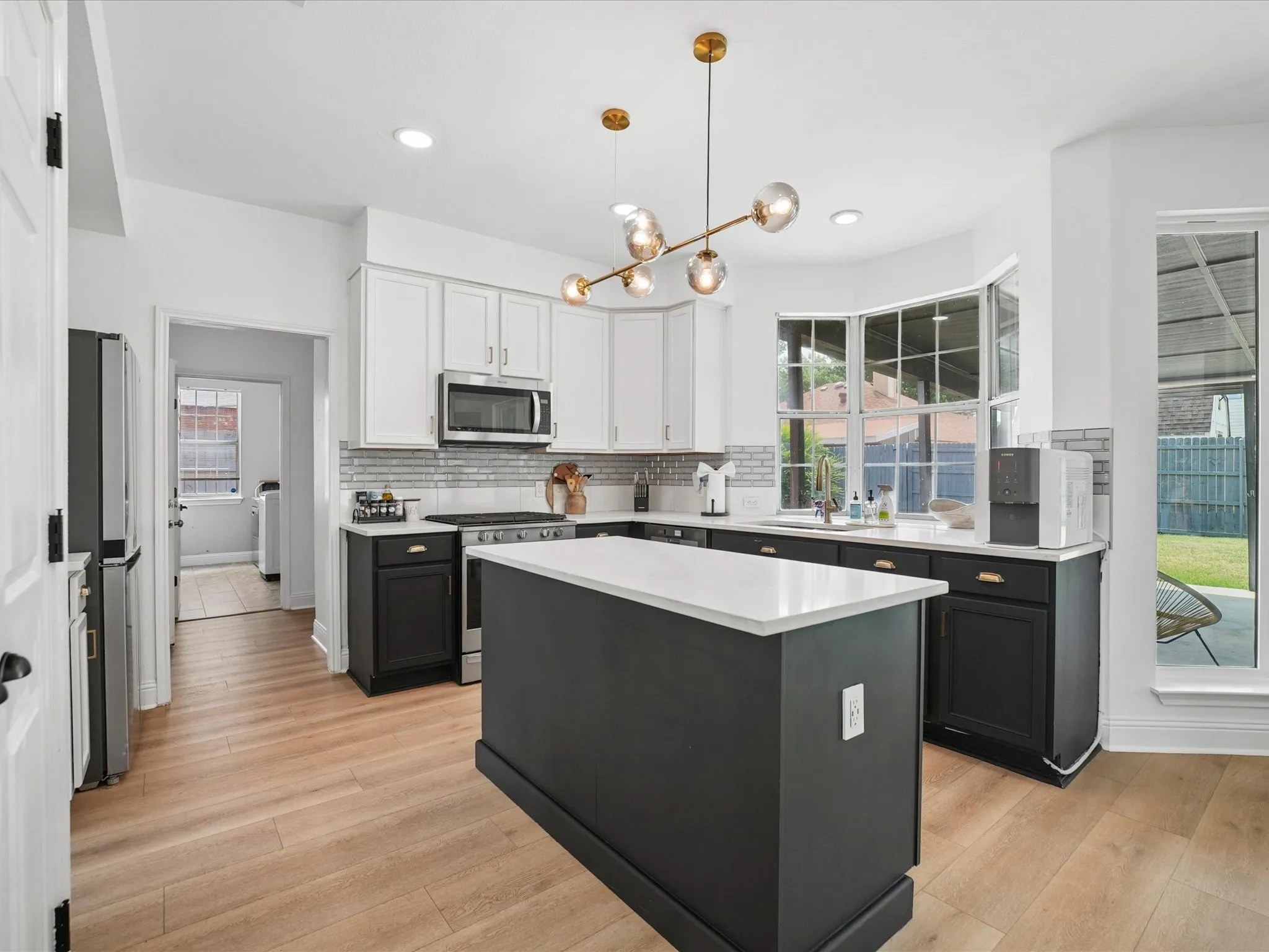 Modern kitchen featuring a central island with a white countertop, two-tone cabinetry, stainless steel appliances, wood-finish flooring, and a contemporary chandelier