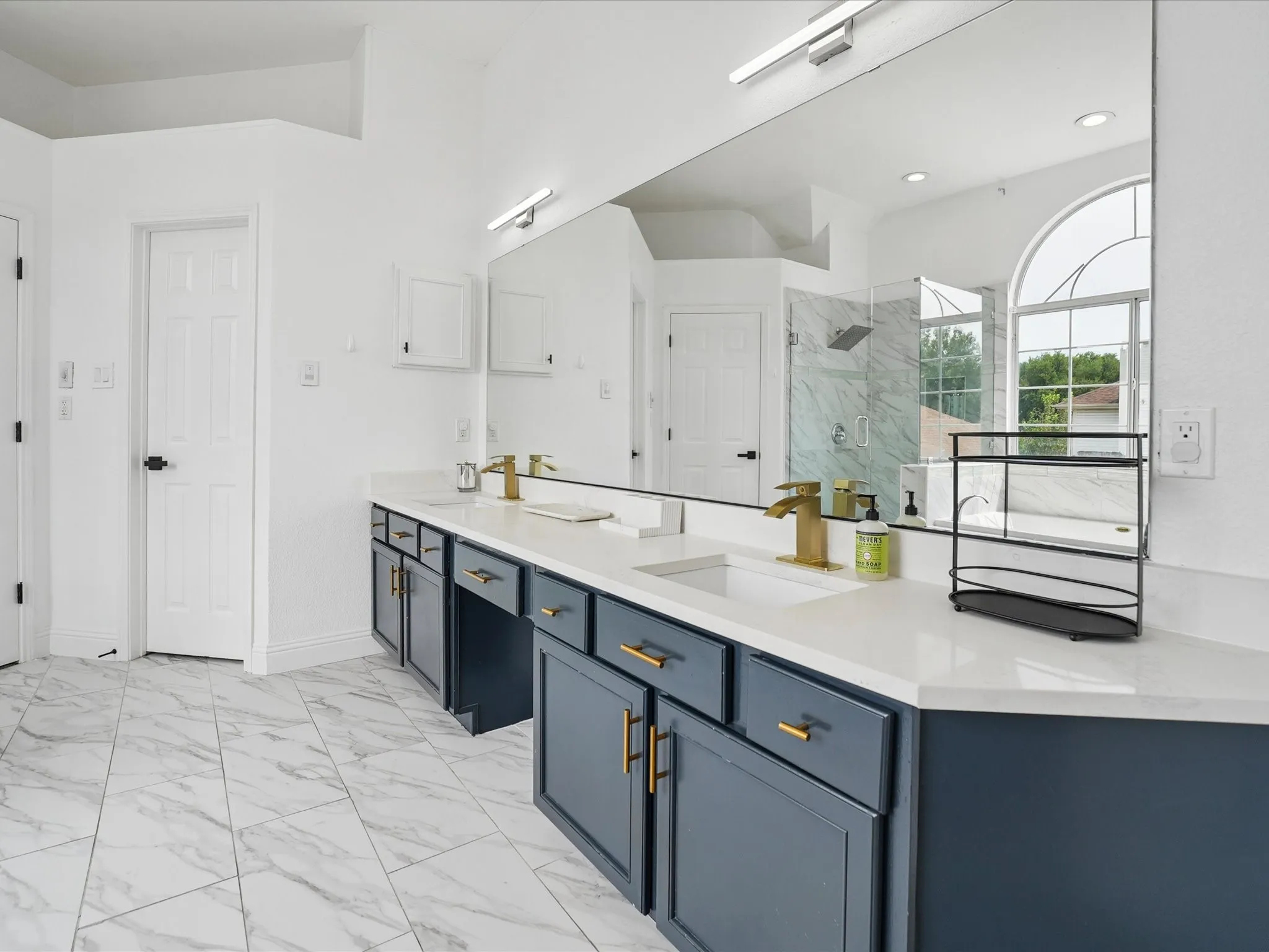 Spa-inspired primary bathroom showcasing a dual-vanity layout with white quartz countertops, an oversized framed mirror, and brass hardware