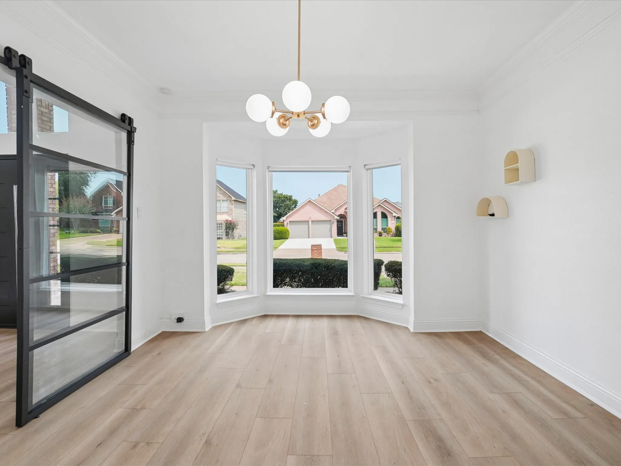 Bright and airy living space showcasing expansive bay windows with natural light, light wood-finish flooring throughout, and a modern pendant light fixture