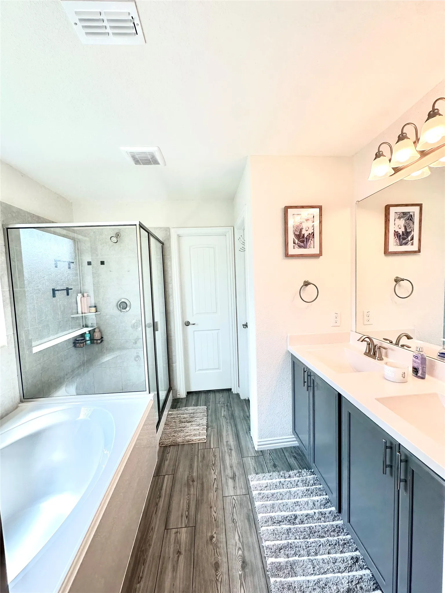 Thoughtfully designed for both functionality and relaxation, the owner's suite bathroom features dual undermount sinks, attractive wood-inspired flooring, a glass-enclosed shower, and a luxurious soaking tub.