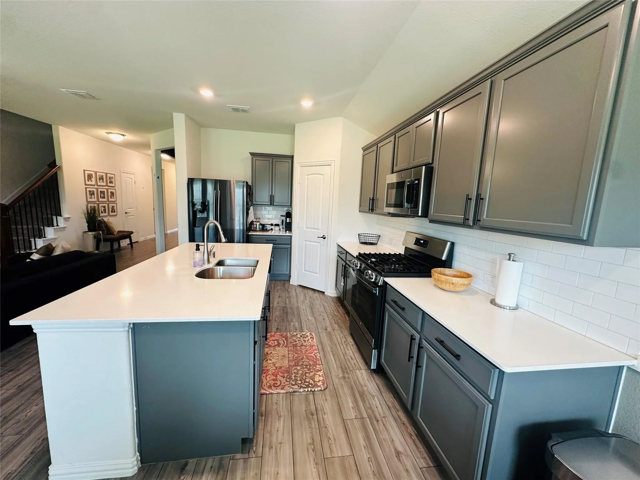 The heart of the home is this stunning kitchen, featuring a large island with seating, gray shaker-style cabinetry, stainless steel appliances, white subway tile backsplash, and durable wood-finish flooring.