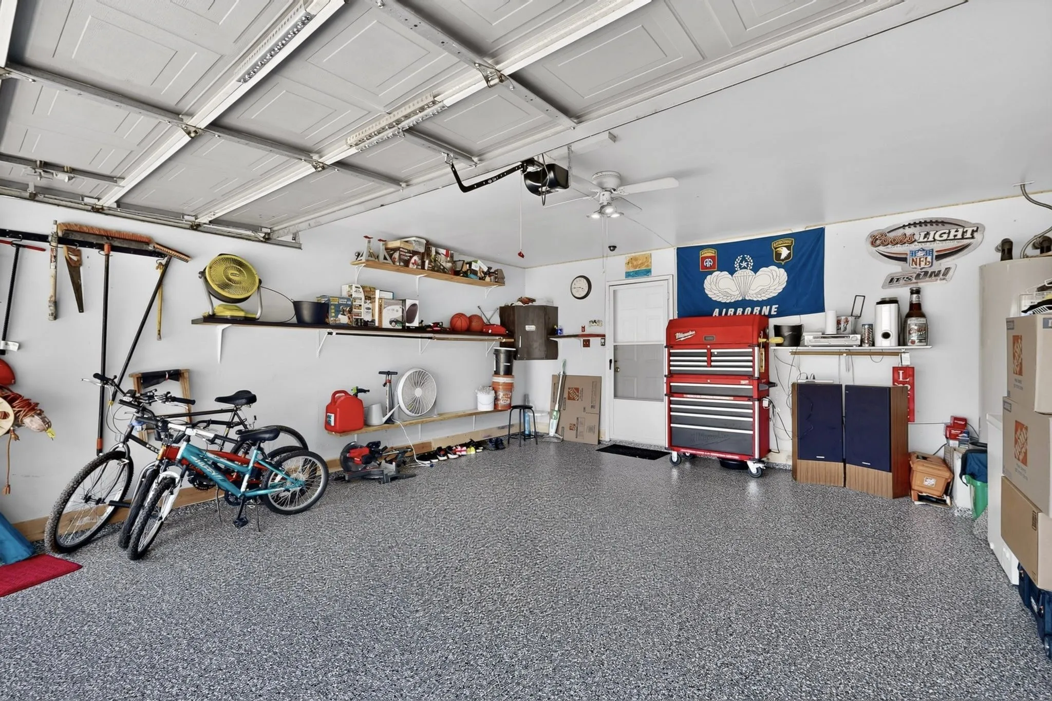 Spacious garage featuring epoxy-coated flooring, extensive wall-mounted storage shelving, built-in tool cabinetry with multiple drawers, integrated workbench area, and ample overhead lighting for functionality and visibility