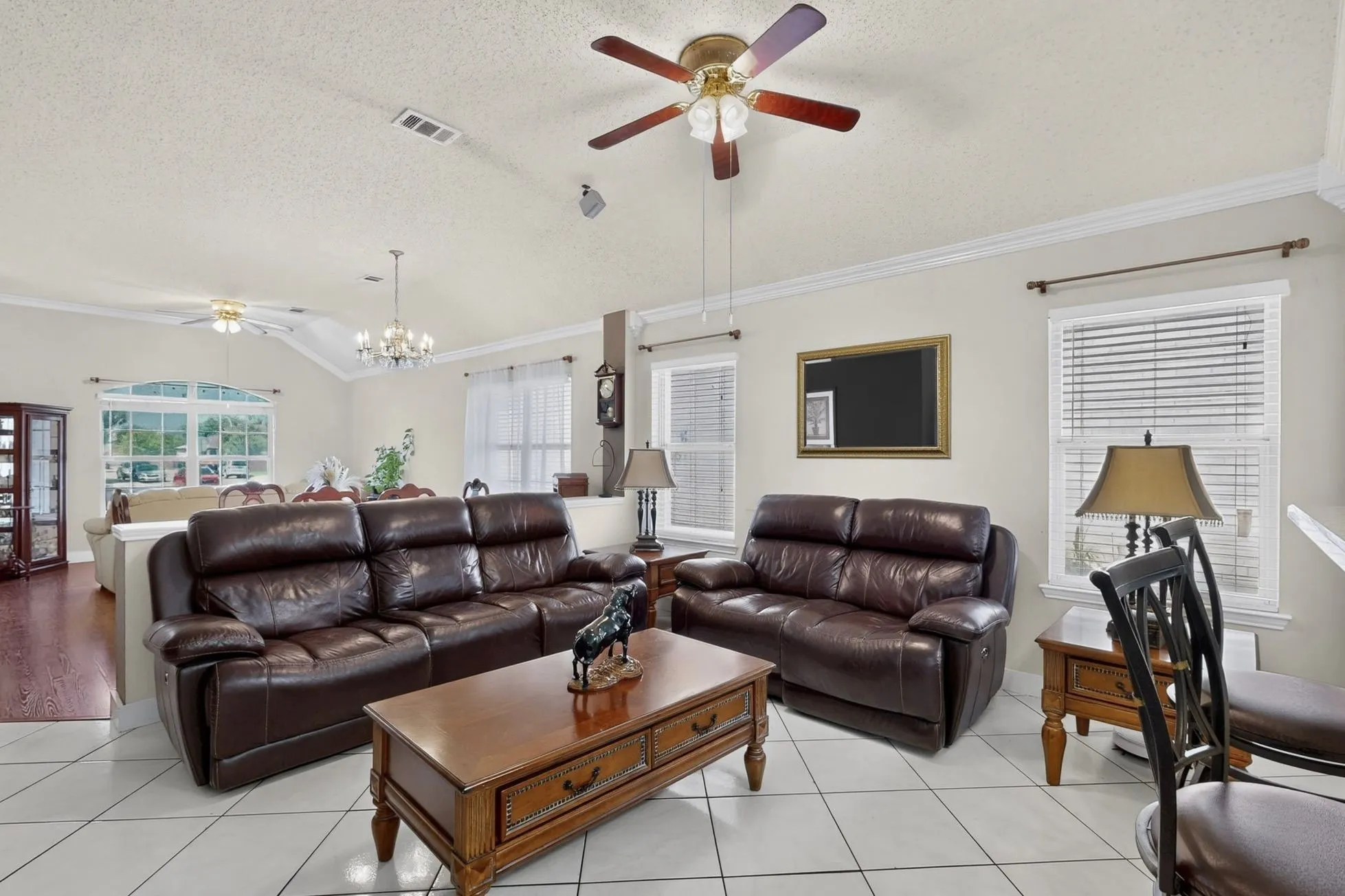 Spacious living area showcasing dual leather sectional seating, ceramic tile flooring, and vaulted ceilings with ceiling fan