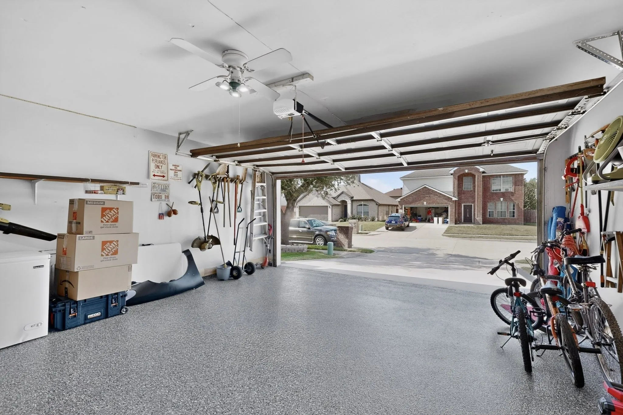 Garage with epoxy-coated flooring, overhead lighting, an exposed ceiling fan, wall-mounted shelving, and an automatic garage door opener