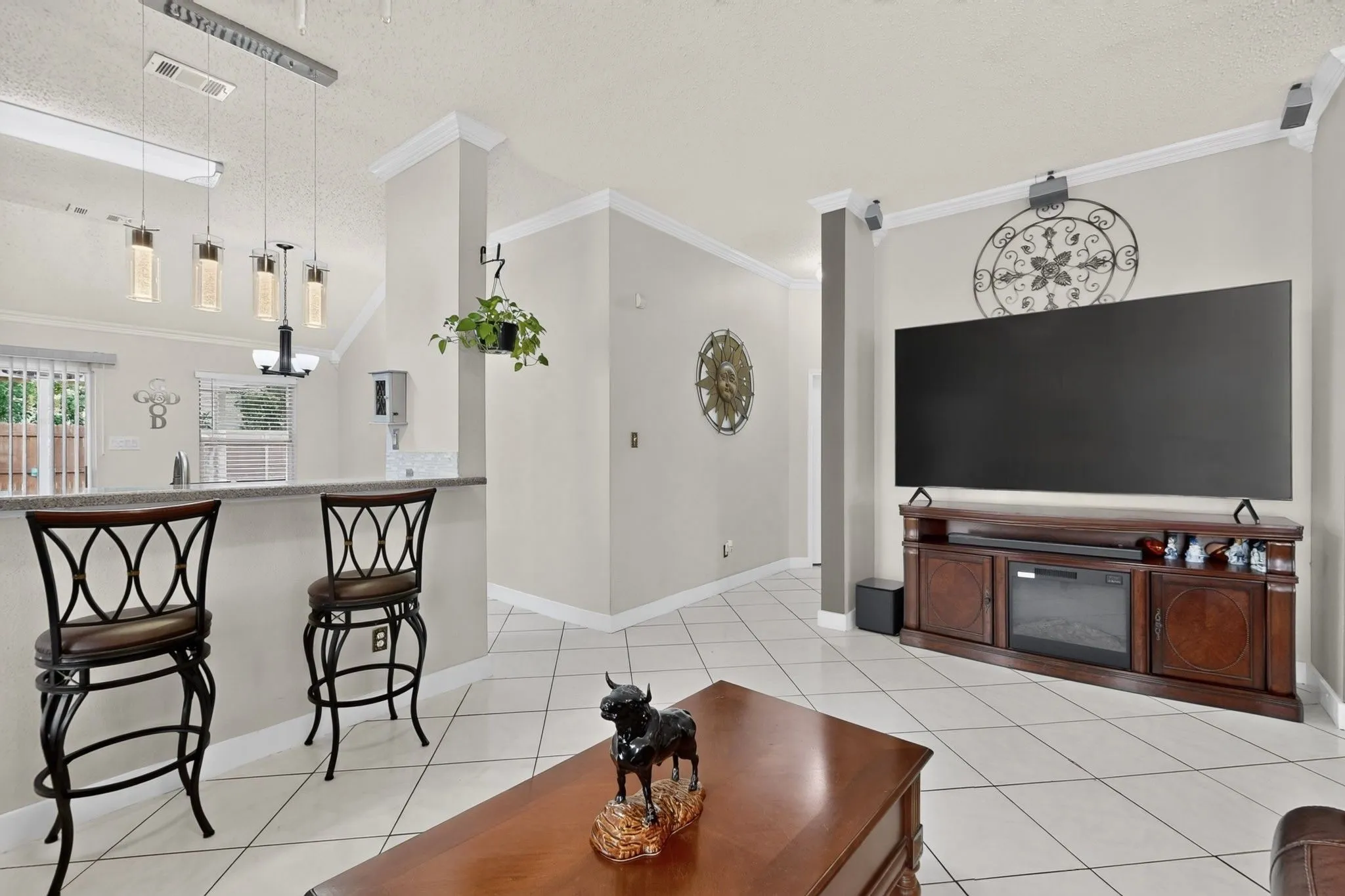 Open-concept living space featuring soaring cathedral ceilings, tile flooring throughout, and a wood-finish entertainment center with built-in fireplace insert