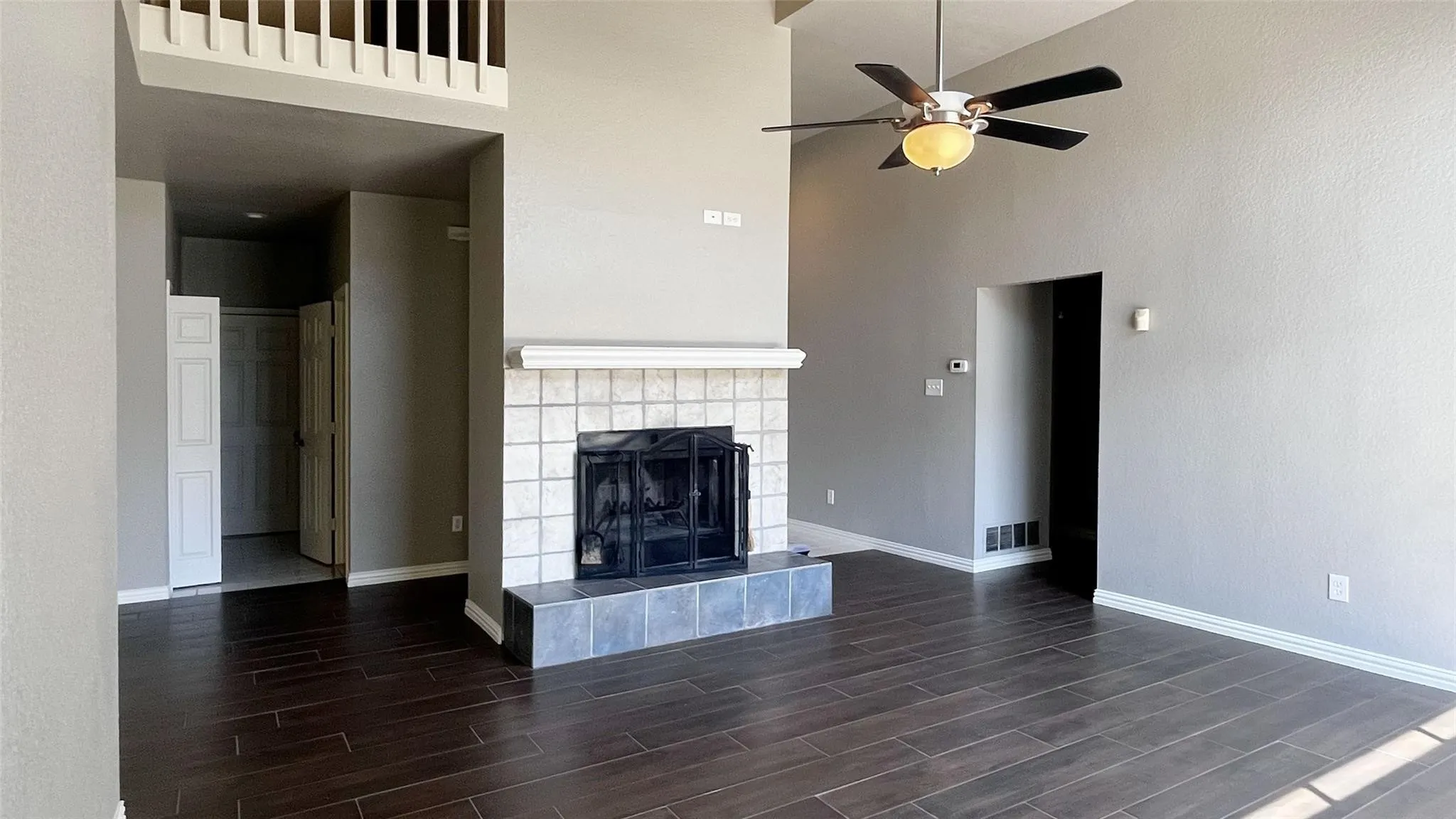 Vaulted ceilings, wood-finish flooring, a ceiling fan with integrated lighting, and a fireplace with a tile surround and hearth