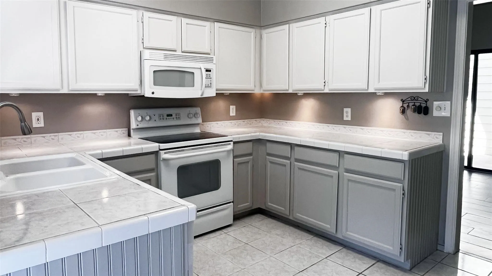 Kitchen featuring white upper cabinetry, gray lower cabinetry, tile countertops, a double basin sink, and tile flooring
