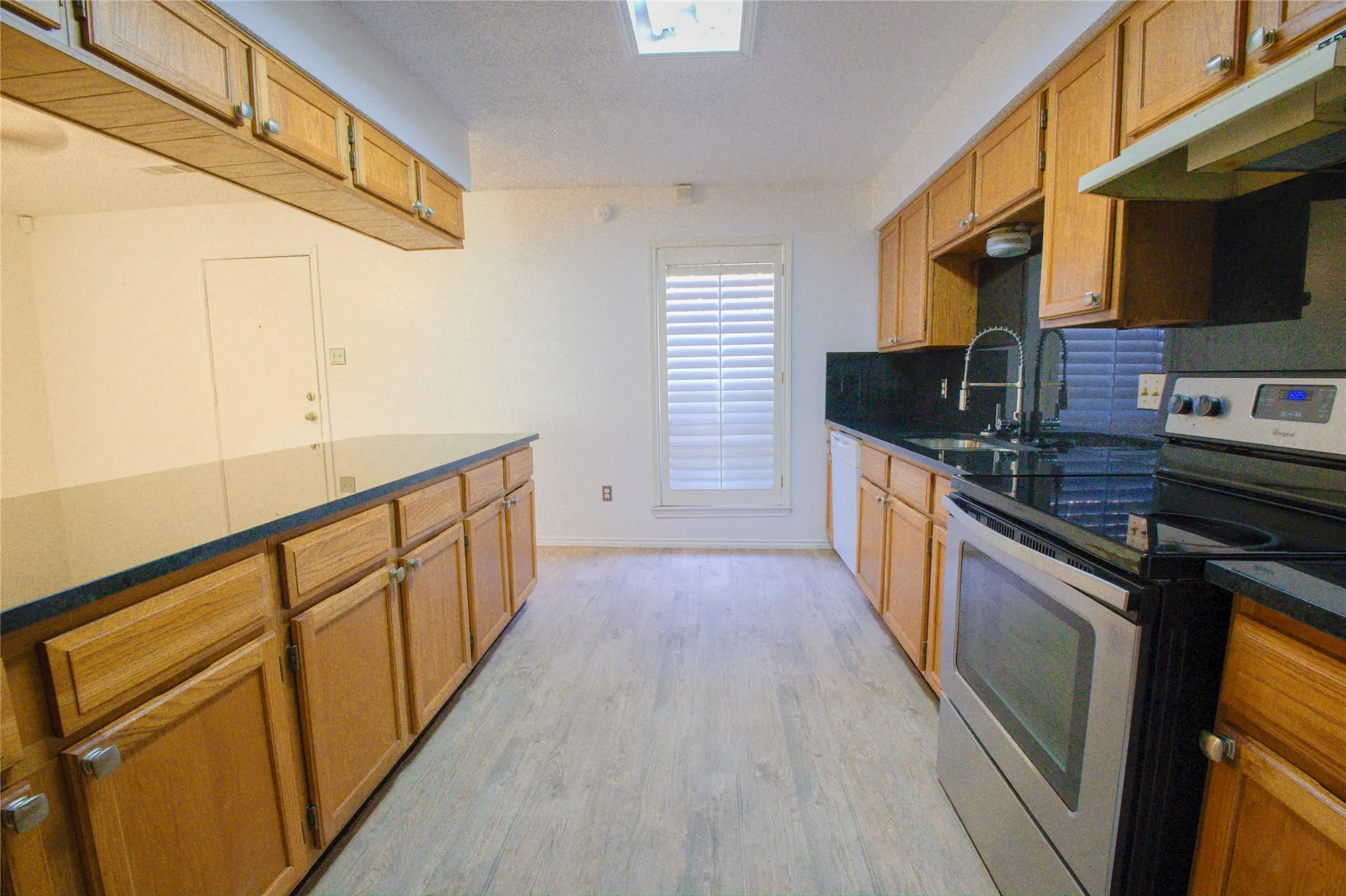 Kitchen featuring wood-finish cabinetry, black countertops, stainless steel appliances, and wood-finish flooring