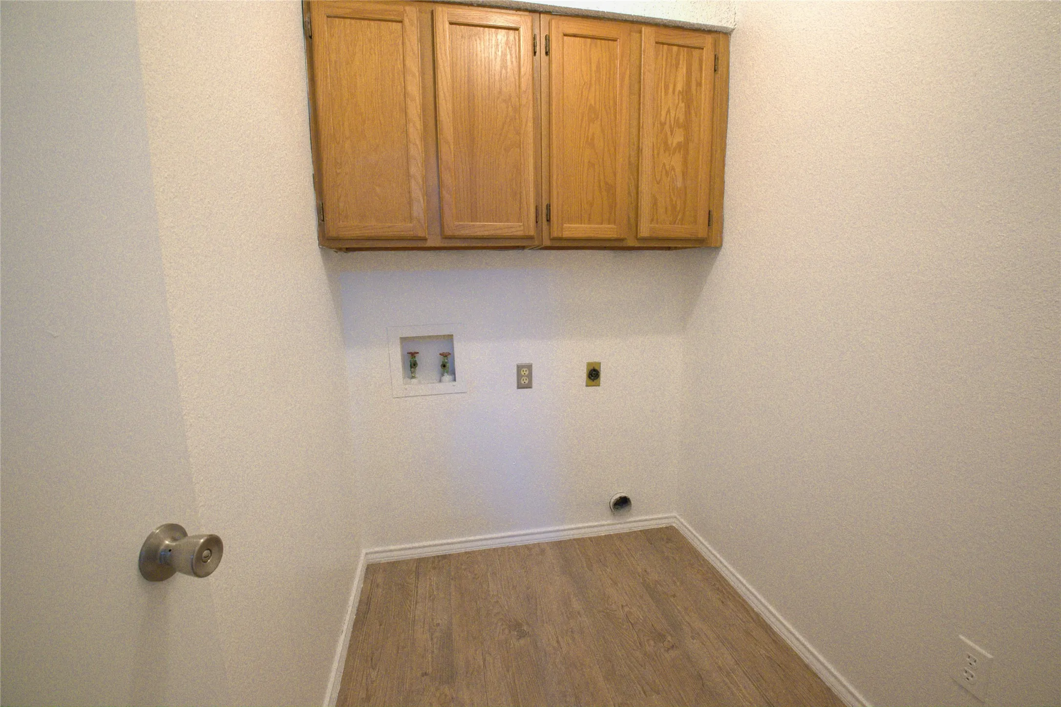 Laundry area with wood-finish flooring, white walls, and built-in upper cabinetry
