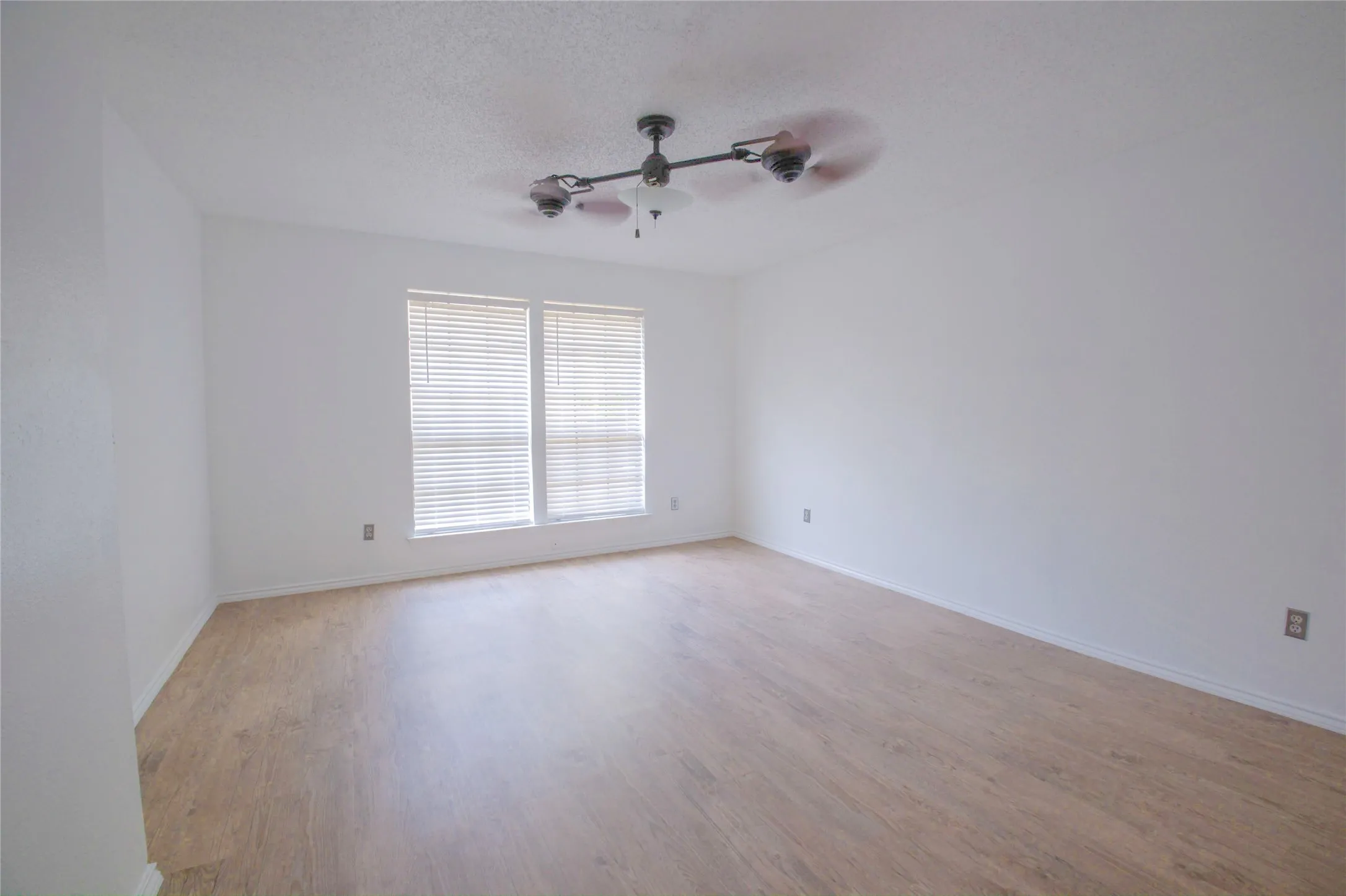Two windows with blinds, wood-finish flooring, and a ceiling fan with integrated lighting