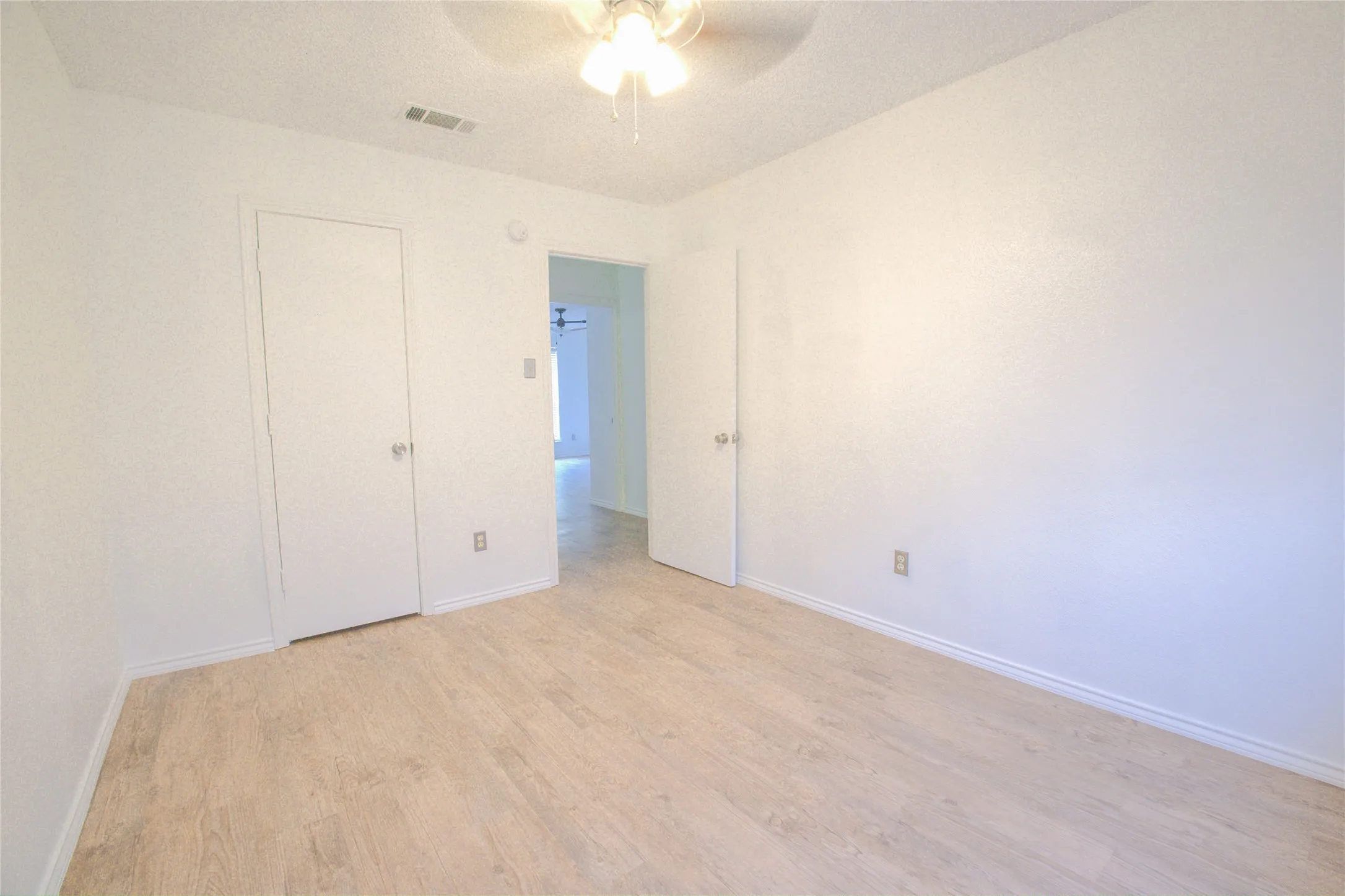 Neutral wall paint, wood-finish flooring, ceiling fan with light fixture, and white interior doors