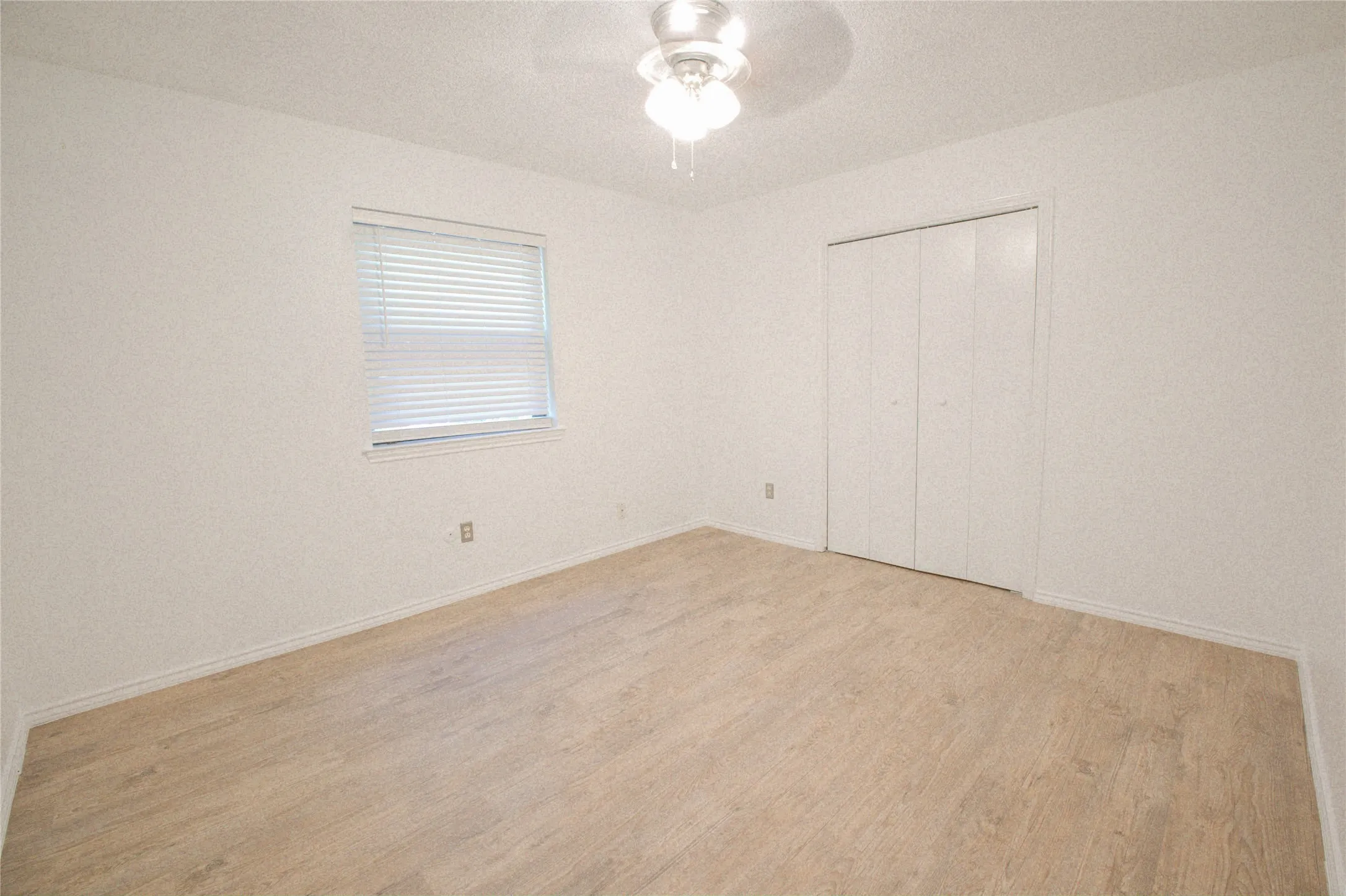 Neutral wall color, wood-finish flooring, ceiling fan with light fixture, window with blinds, and bi-fold closet doors