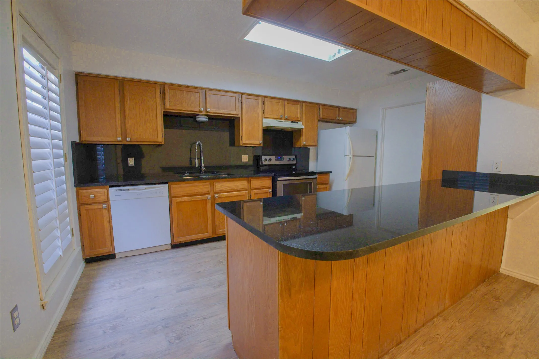 Kitchen featuring wood cabinetry, dark stone countertops, a breakfast bar, and a skylight